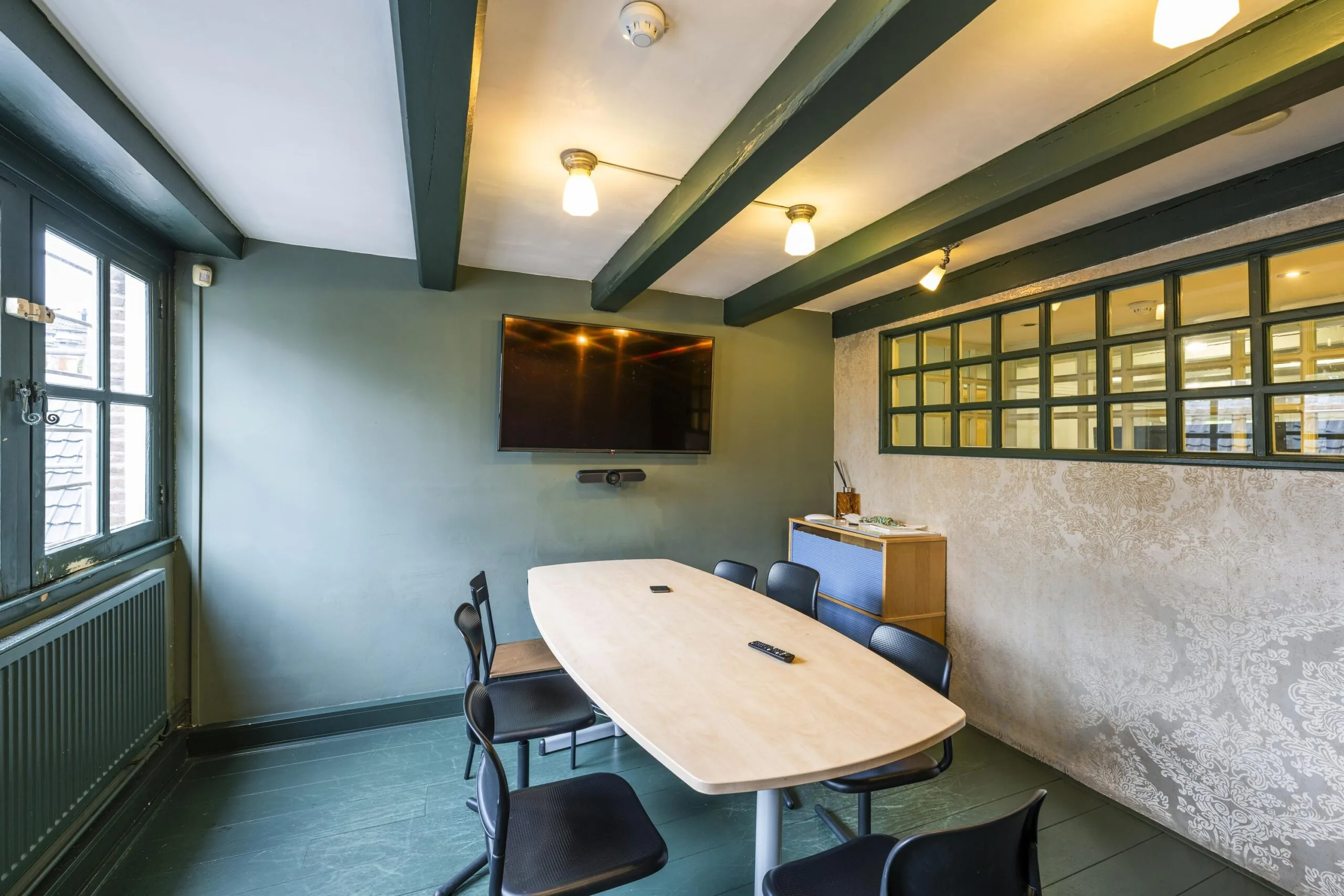 Modern meeting room on Leidsegracht with a large screen, oval table, and exposed ceiling beams.