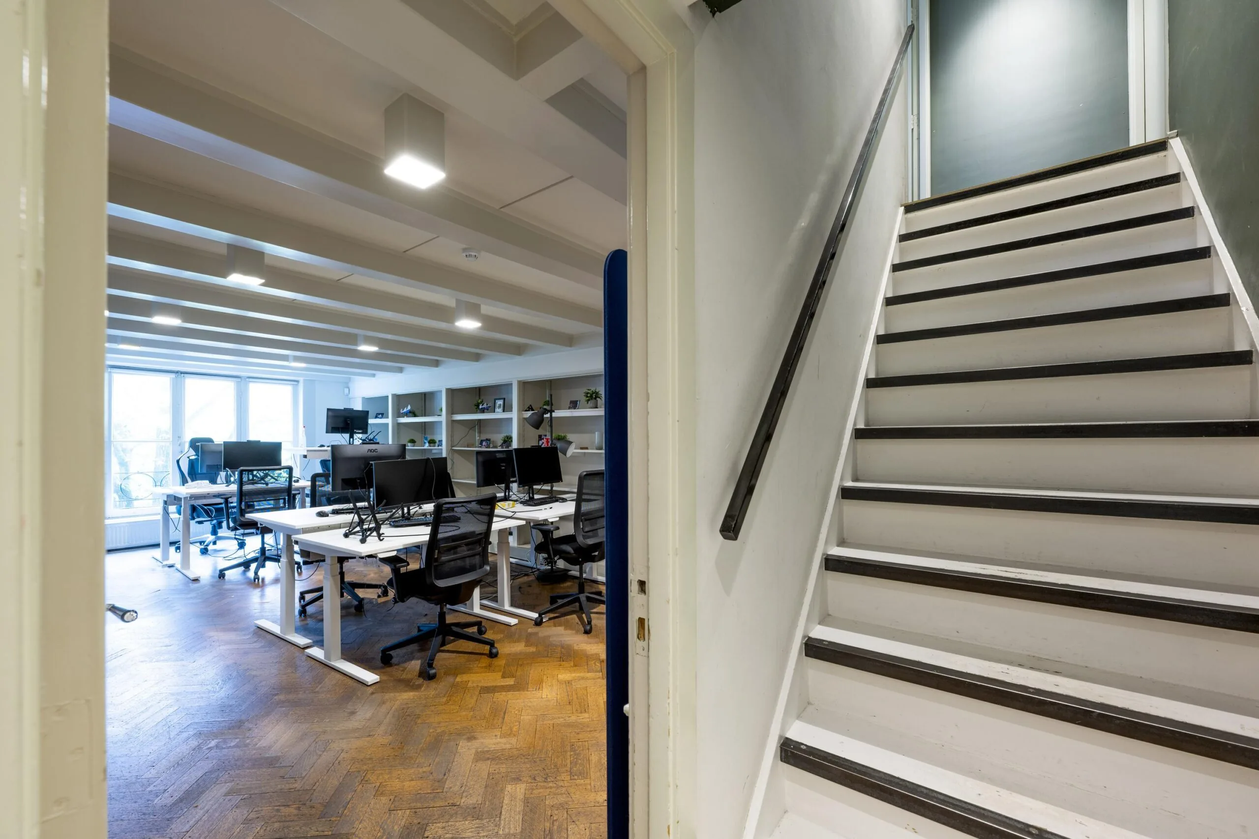 Modern office space with desks and computers next to a white staircase in a building on Leidsegracht.