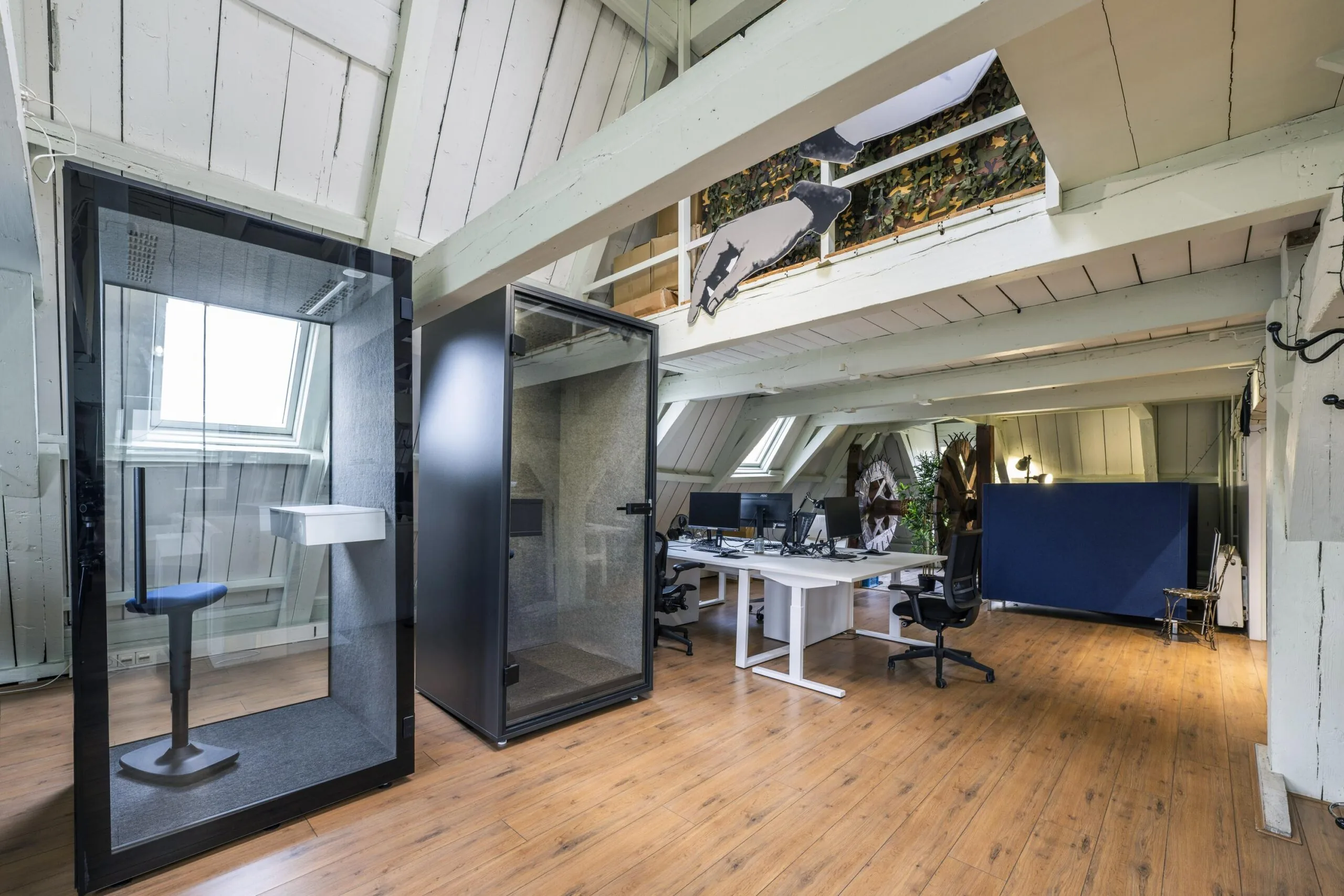 Modern attic office space on Leidsegracht with workstations, phone booths, and wooden flooring under a white-beamed ceiling.