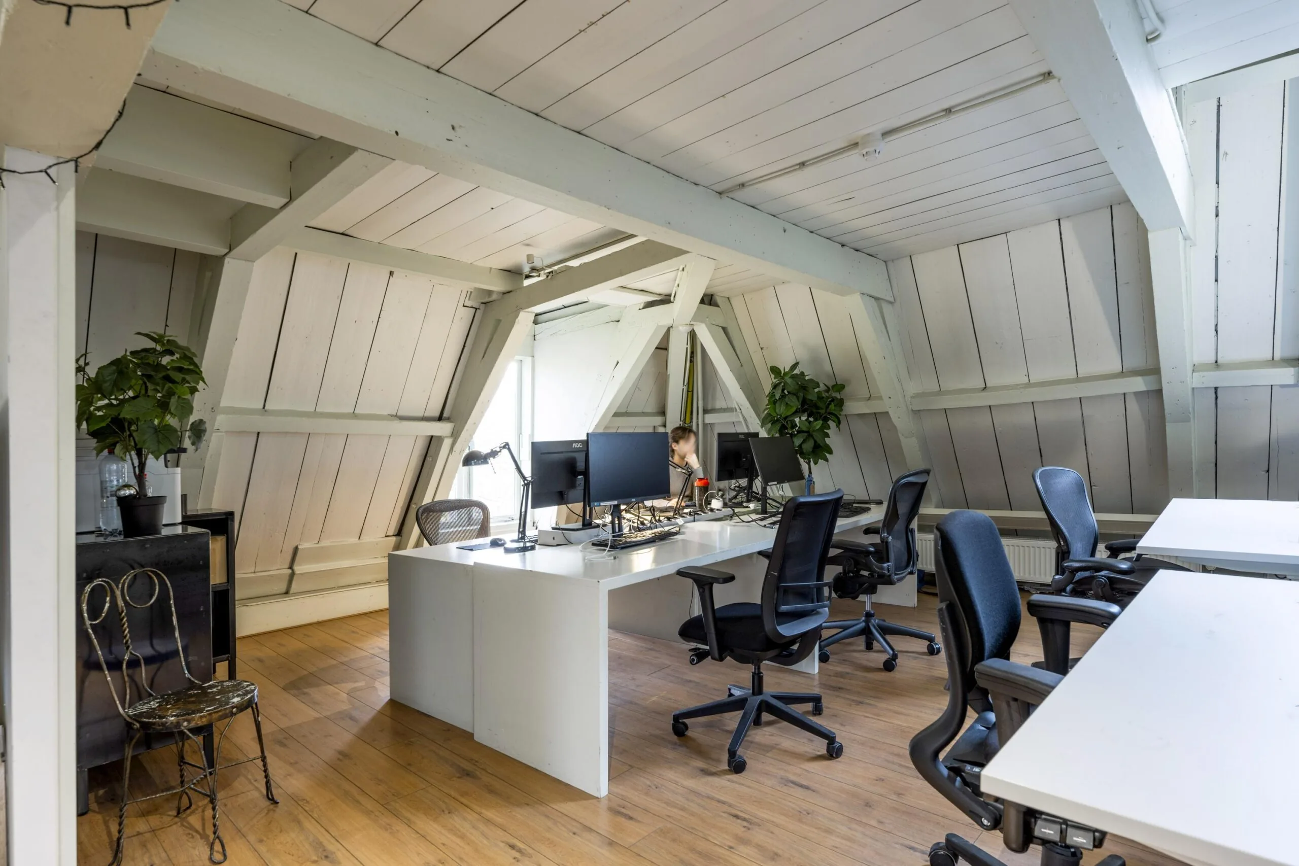 Modern attic office space on Leidsegracht with wooden floors, white beams, desks, and ergonomic chairs.