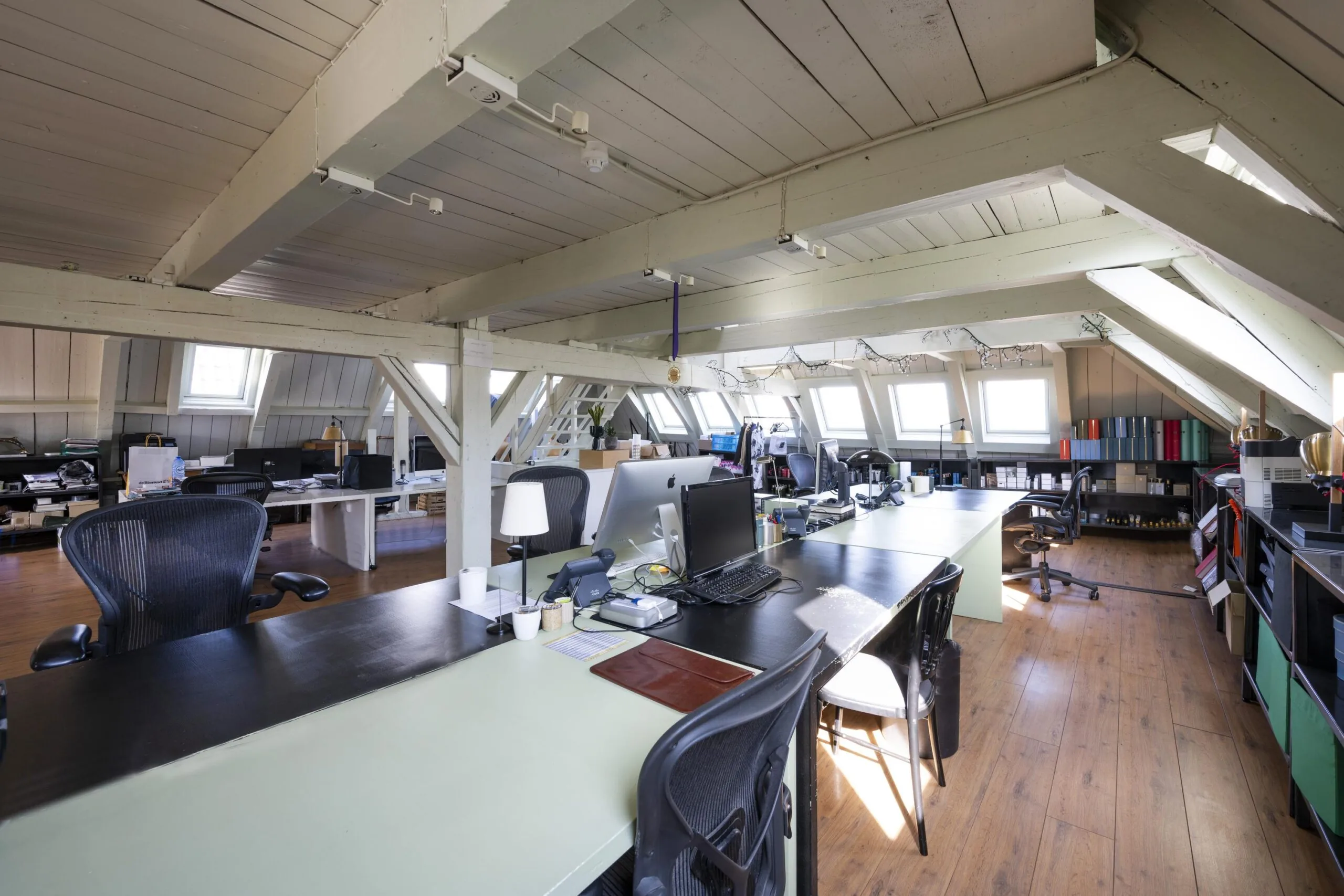 Modern attic office space on Leidsegracht with wooden beams, shared desks, and natural light from skylight windows.
