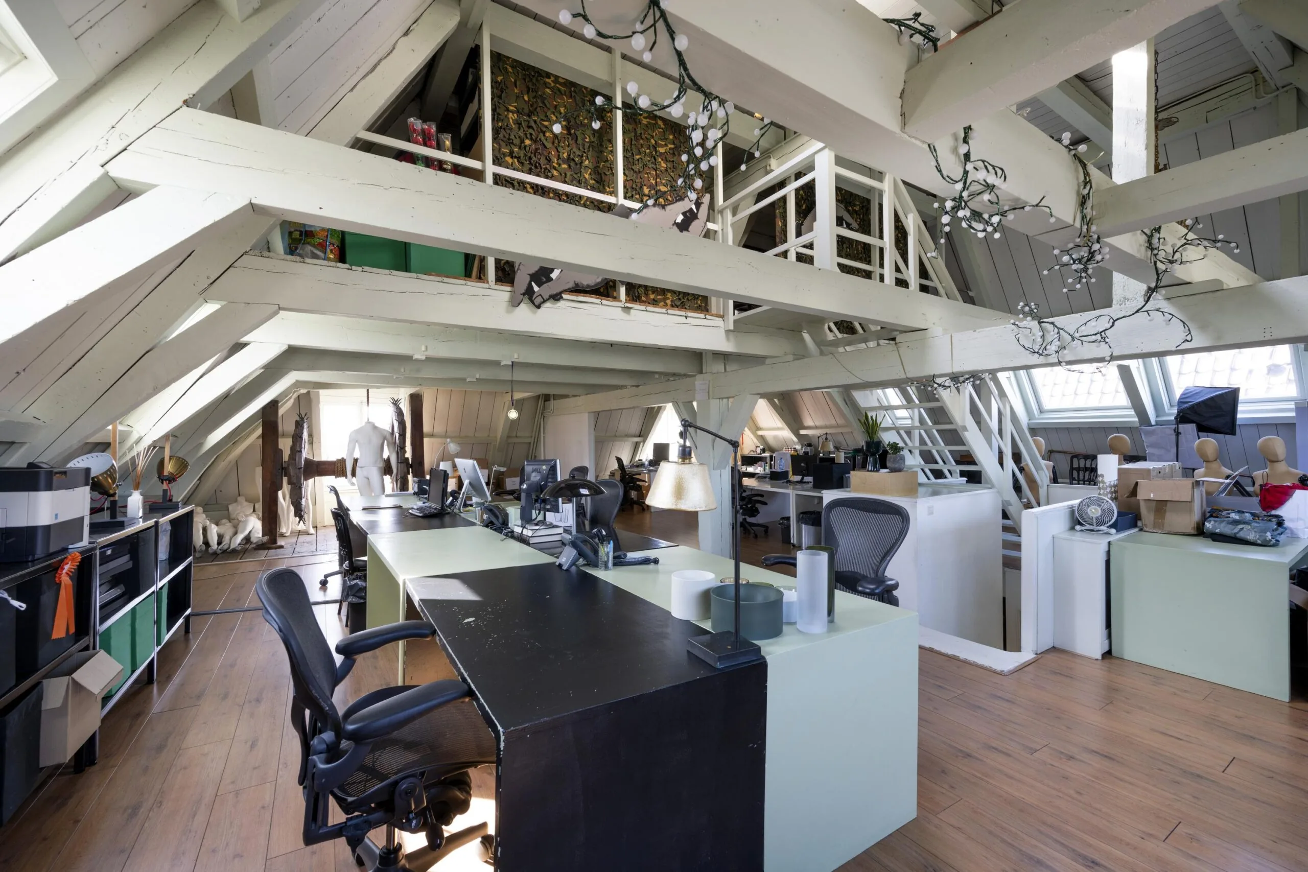 Modern attic office space on Leidsegracht with exposed wooden beams, desks, mannequins, and creative decor.
