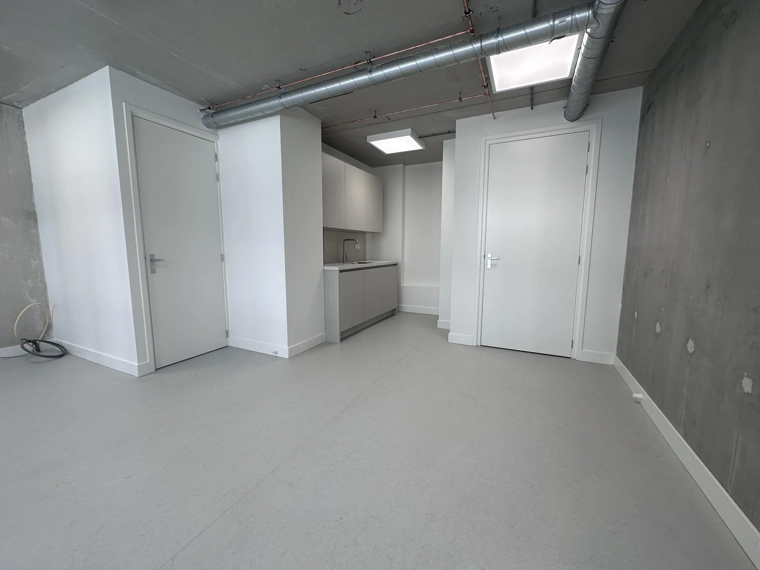 Minimalist modern studio interior on Willem Parelstraat with a small kitchen, white doors, and exposed ventilation pipes.