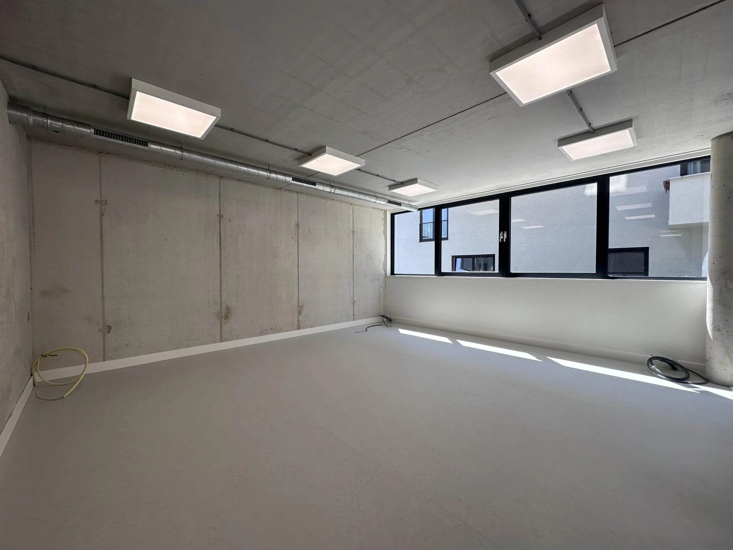 Empty office space on Willem Parelstraat with concrete walls, large windows, and ceiling lights.