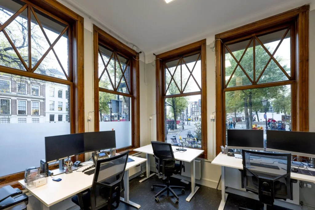 Modern office workspace with large wooden-framed windows overlooking Westermarkt square in Amsterdam.