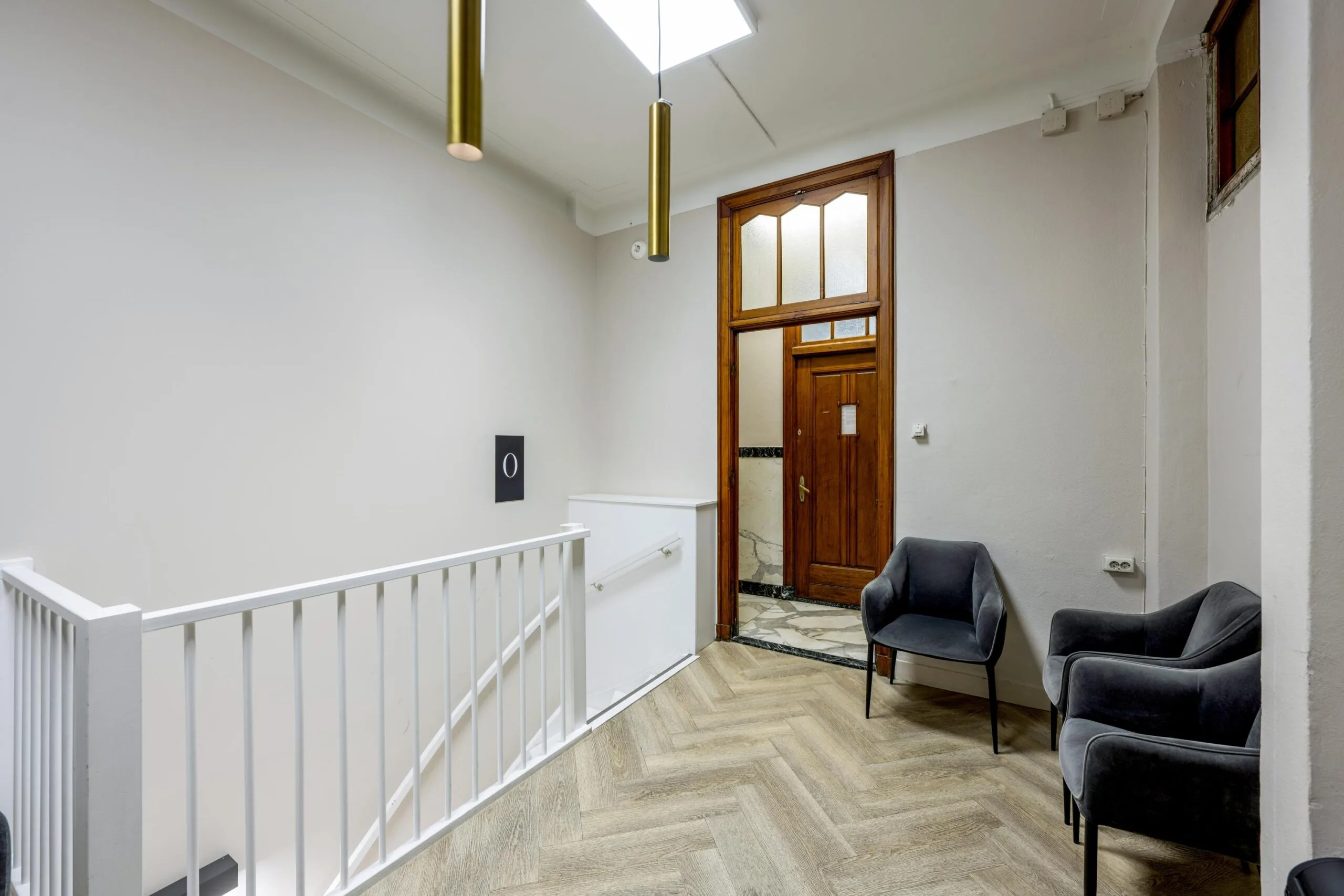 Modern hallway interior with two velvet chairs, a wooden door, and gold pendant lights at Westermarkt.
