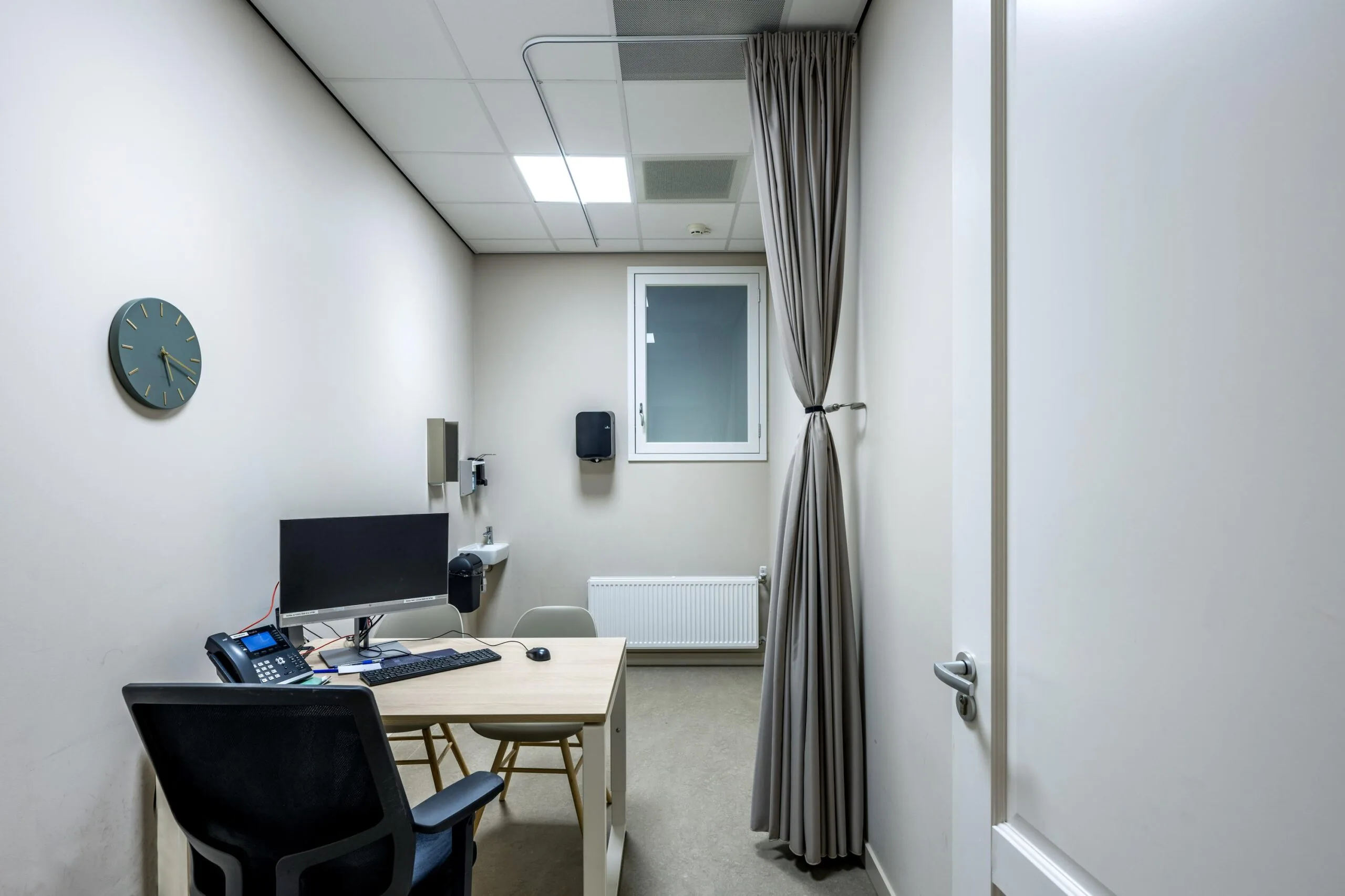 Modern medical consultation room at Westermarkt with a desk, computer, and privacy curtain.