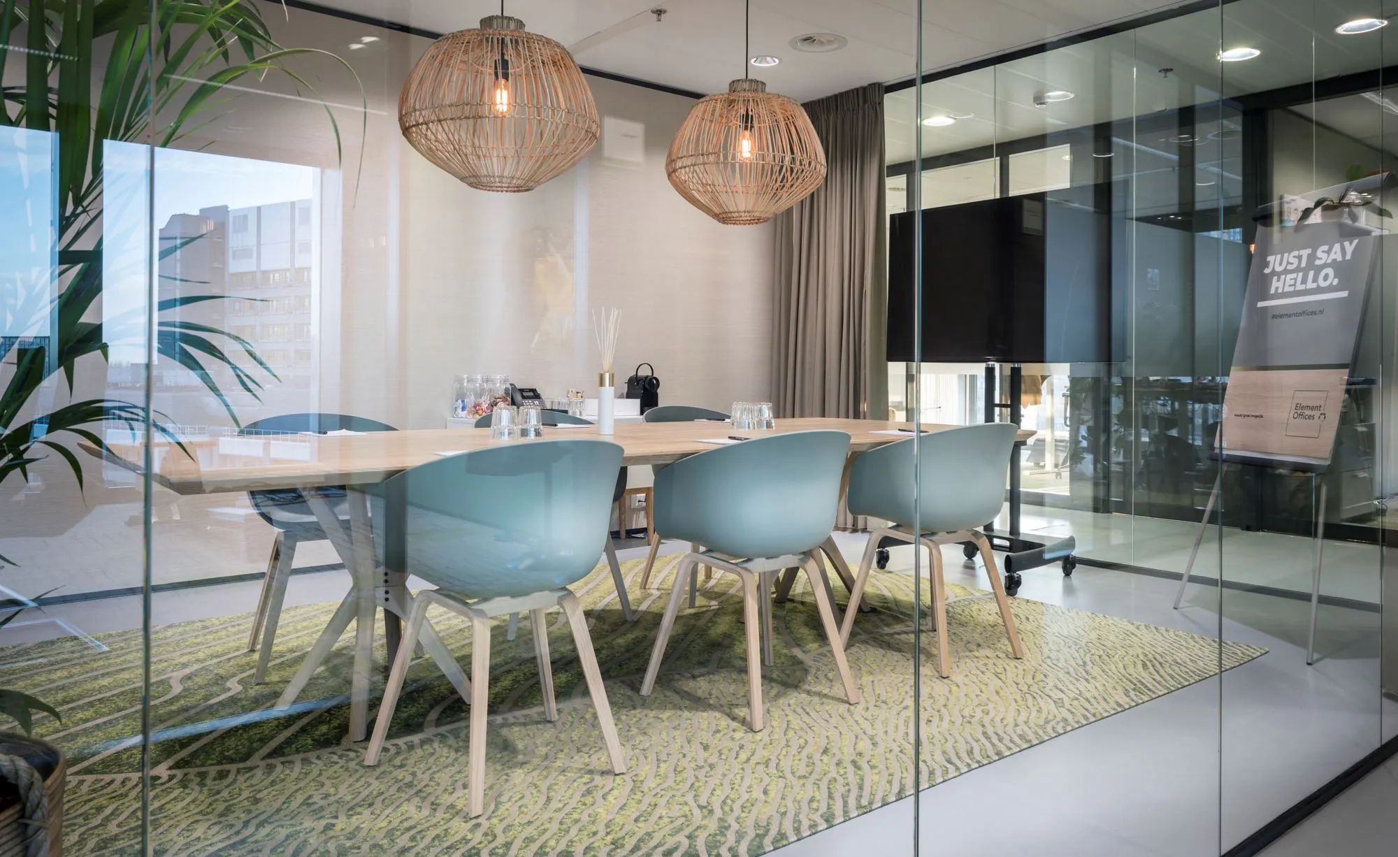 Moderne vergaderruimte met glazen wanden, zes blauwe stoelen, een houten tafel en hanglampen, bij Element Offices.