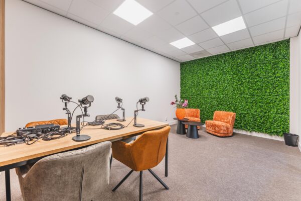 Modern podcast recording room with microphones, a wooden table, and a green plant wall at Paasheuvelweg.