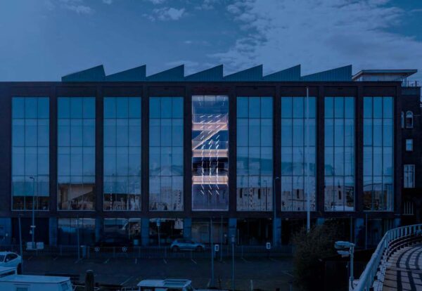 Modern office building on Nieuwe Vaart with large reflective windows and illuminated central staircase.