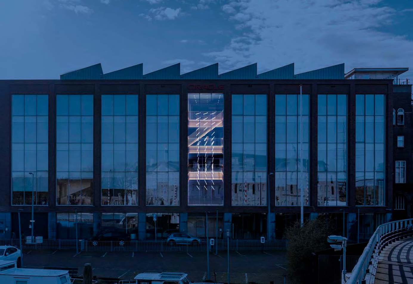 Modern office building on Nieuwe Vaart with large reflective windows and illuminated central staircase.