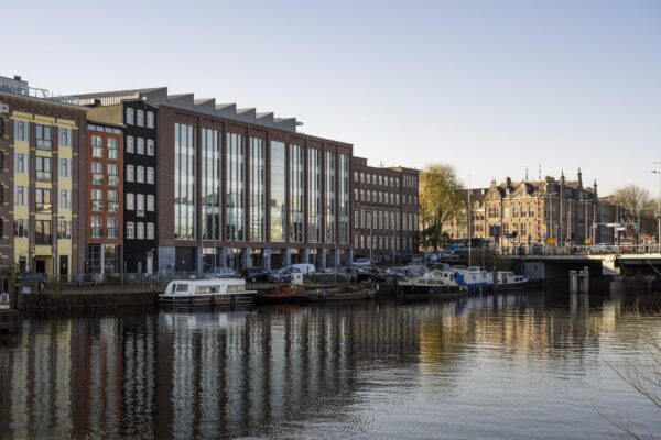 Modern office buildings and moored boats along the Nieuwe Vaart canal in Amsterdam.