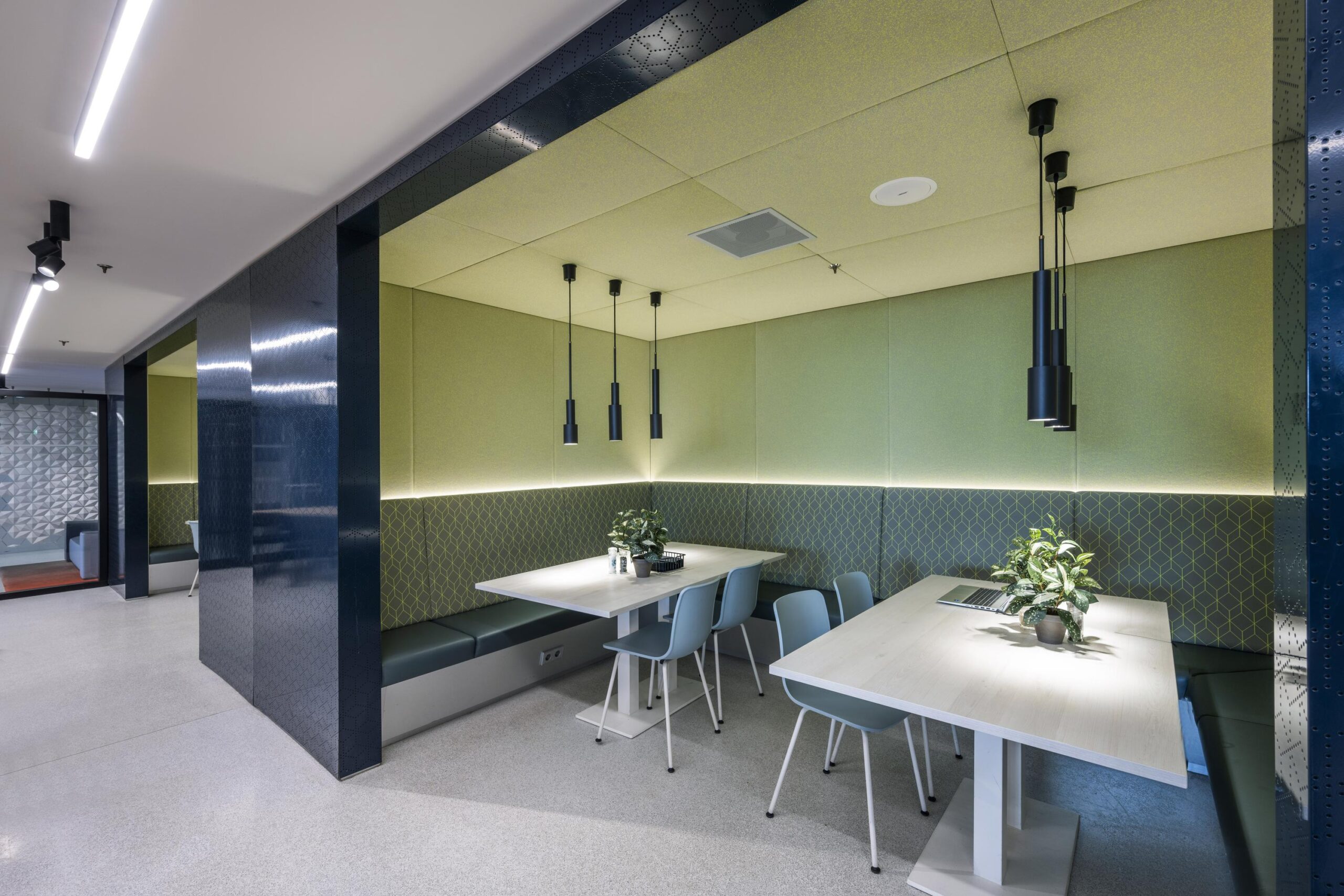 Modern seating area at Nieuwevaart with built-in benches, light wood tables, pendant lighting, and green acoustic wall panels.