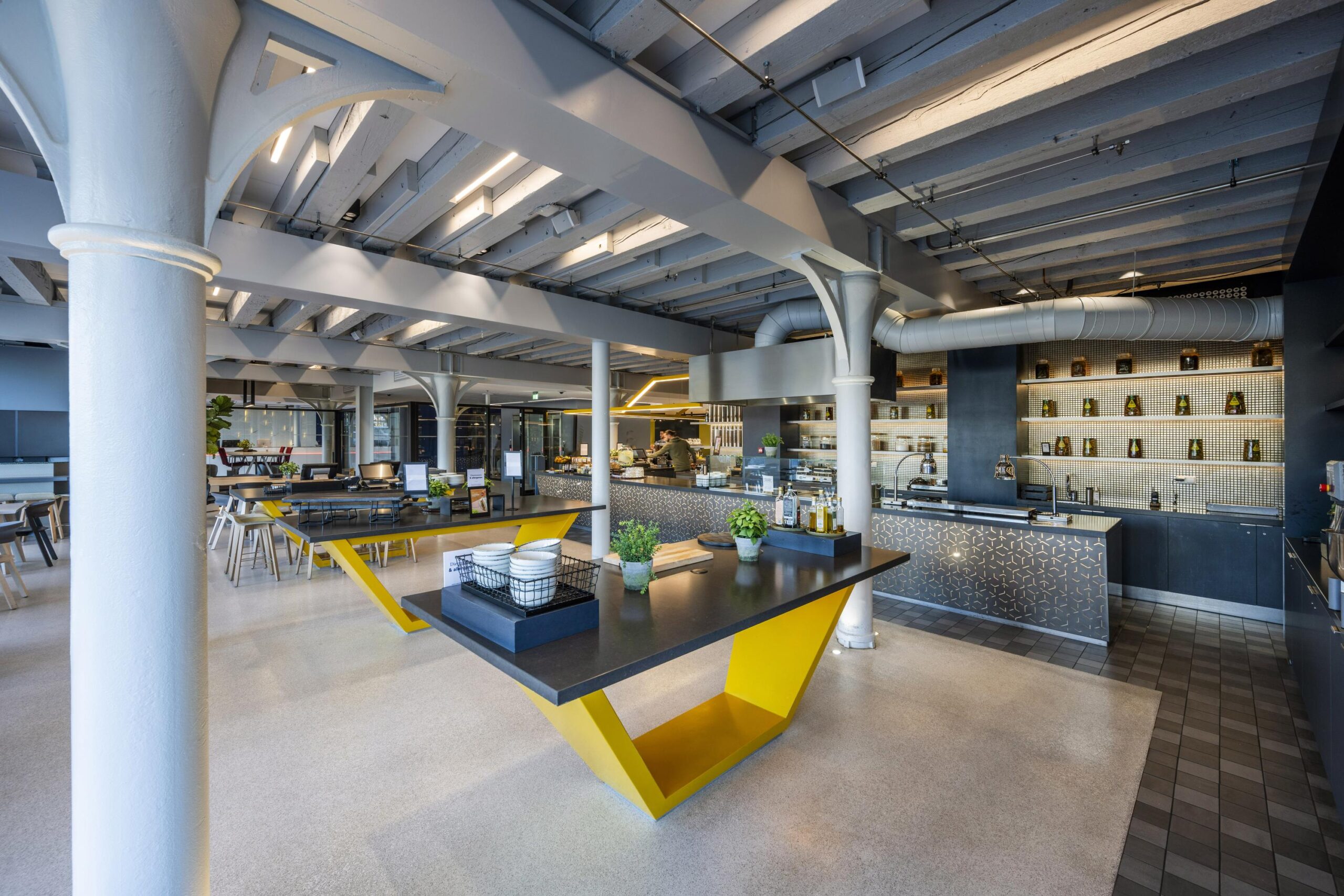 Modern industrial-style cafeteria interior at Nieuwe Vaart with sleek furniture, open ceiling beams, and a stylish food counter.