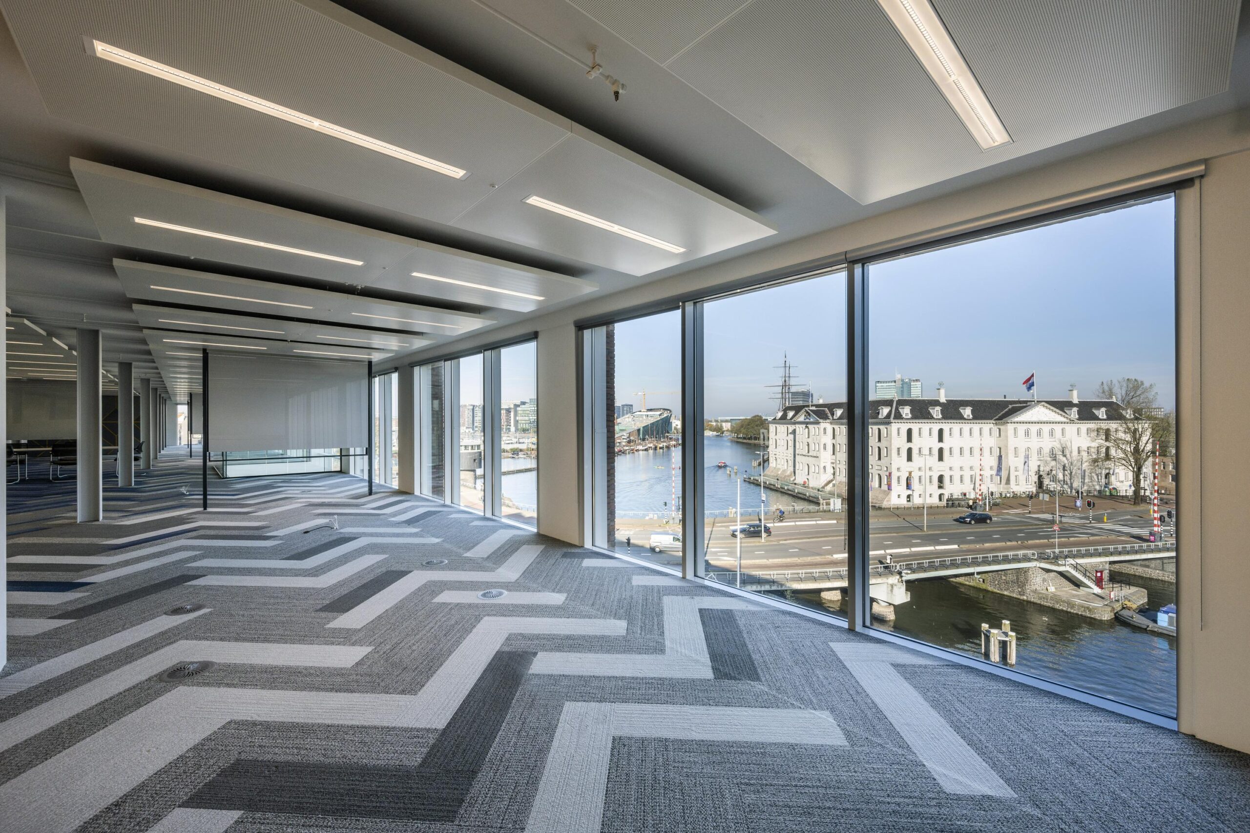Modern office space with large windows offering a view of the Nieuwe Vaart canal and the National Maritime Museum in Amsterdam.