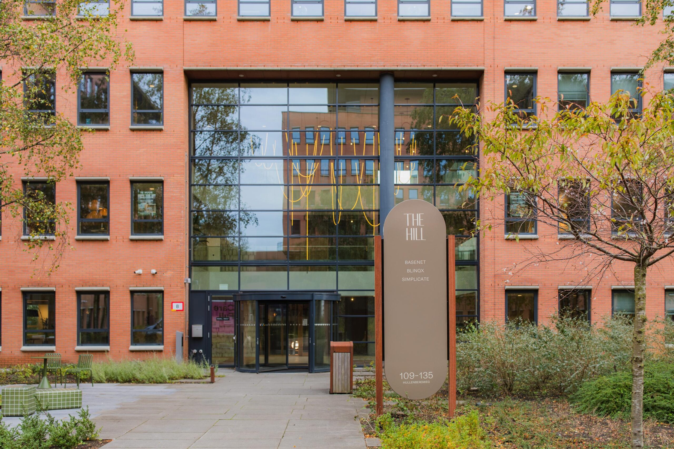 Front view of the office building "The Hill" at Hullenbergweg 109–135 with a sign listing companies including Basenet, Blinxx, and Simplicate.