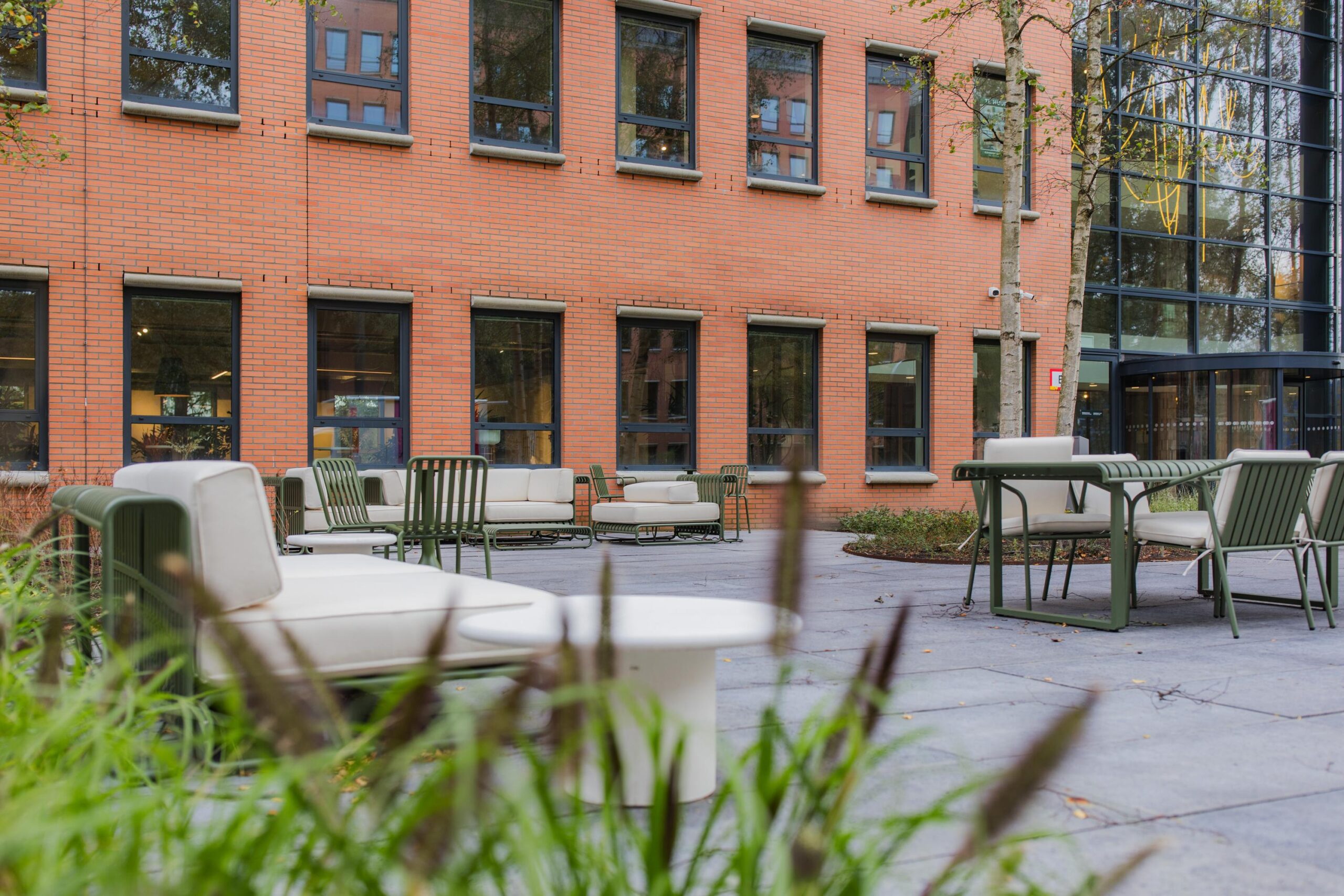 Modern outdoor seating area with green chairs and white cushions in front of a brick office building on Hullenbergweg.