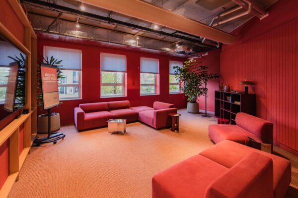Modern red lounge area with comfortable seating, large windows, and industrial ceiling details at Hullenbergweg.