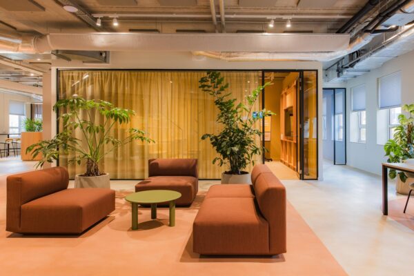 Modern lounge area at Hullenbergweg with terracotta seating, green plants, and a glass-walled meeting space.