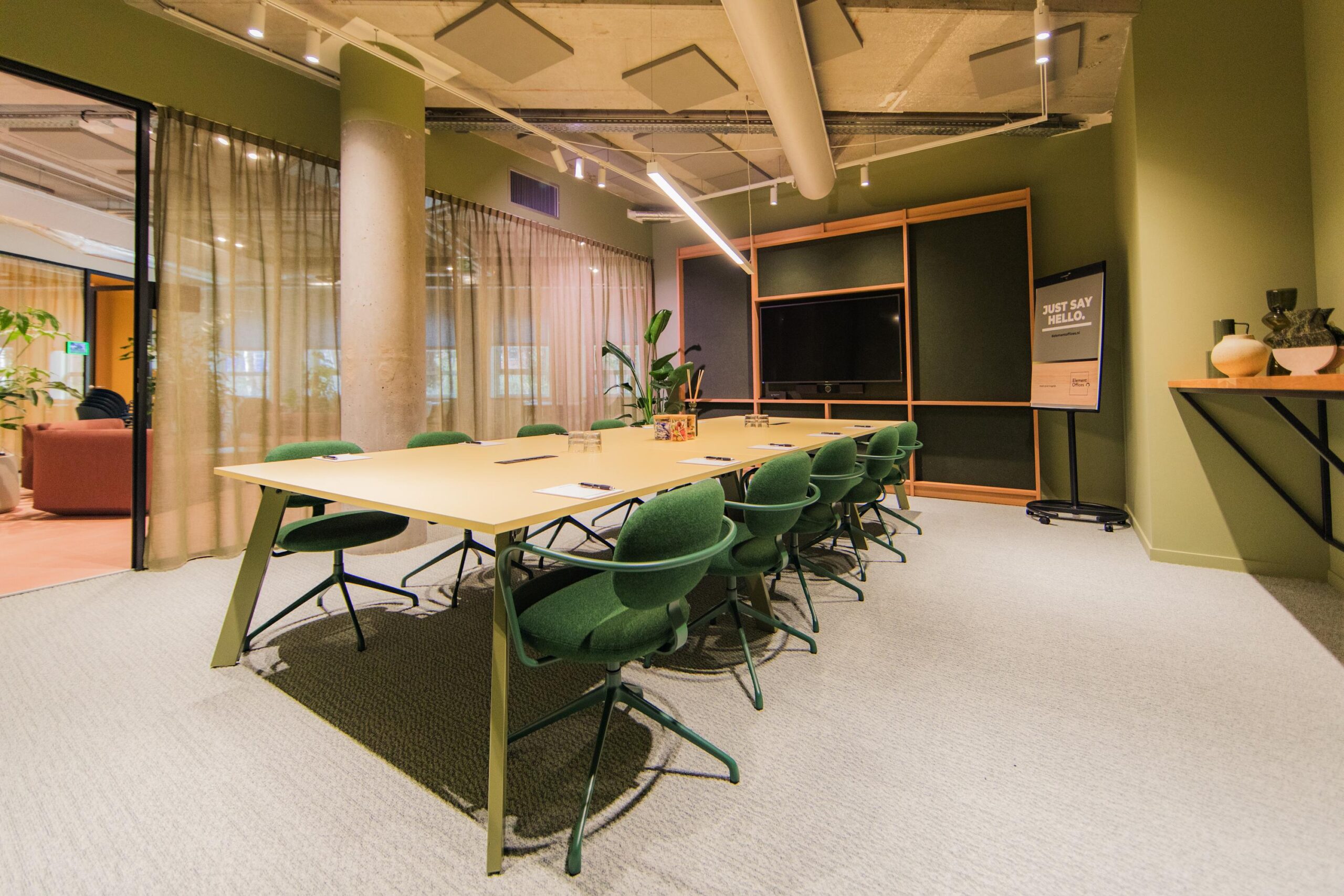Modern conference room at Hullenbergweg with green chairs, a large meeting table, and a presentation screen.