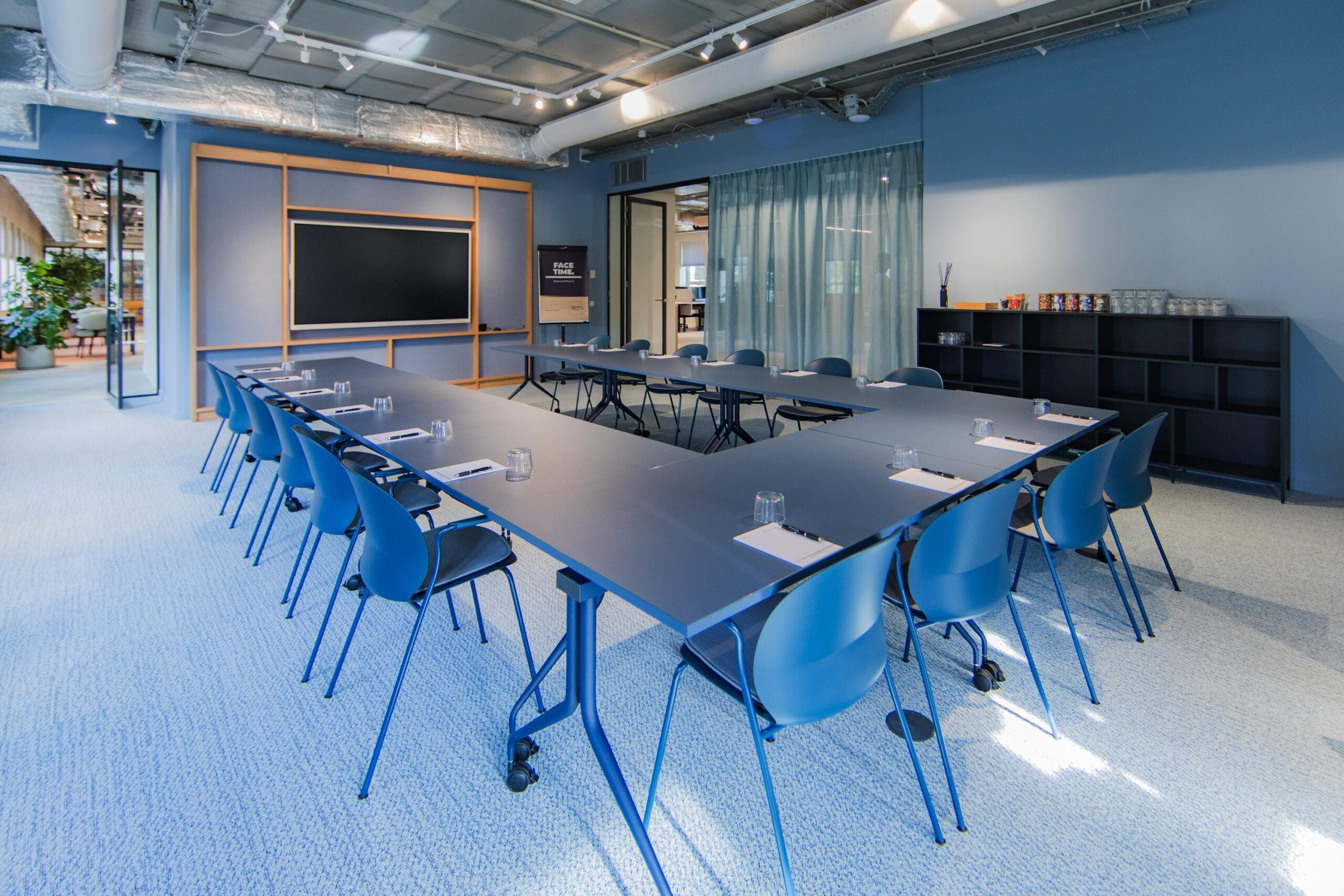 Modern conference room at Hullenbergweg with a U-shaped table setup, blue chairs, and a large presentation screen.