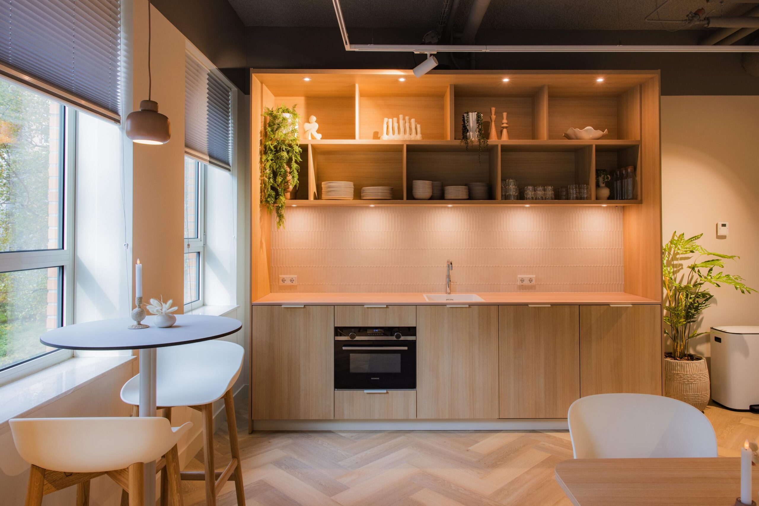 Modern kitchen interior with wooden cabinets, open shelves, and a small dining table by large windows at Hullenbergweg.