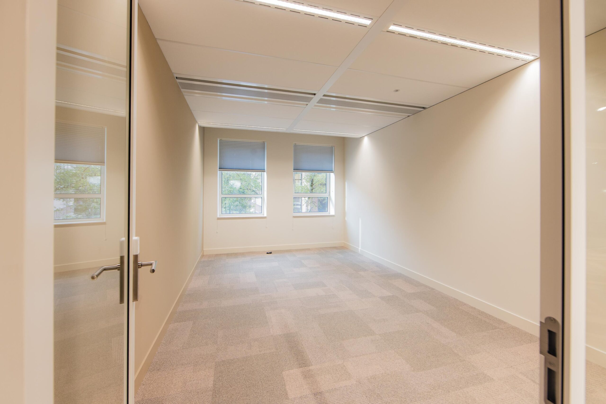 Empty office space at Hullenbergweg with beige walls, carpeted floor, and two windows with blinds.
