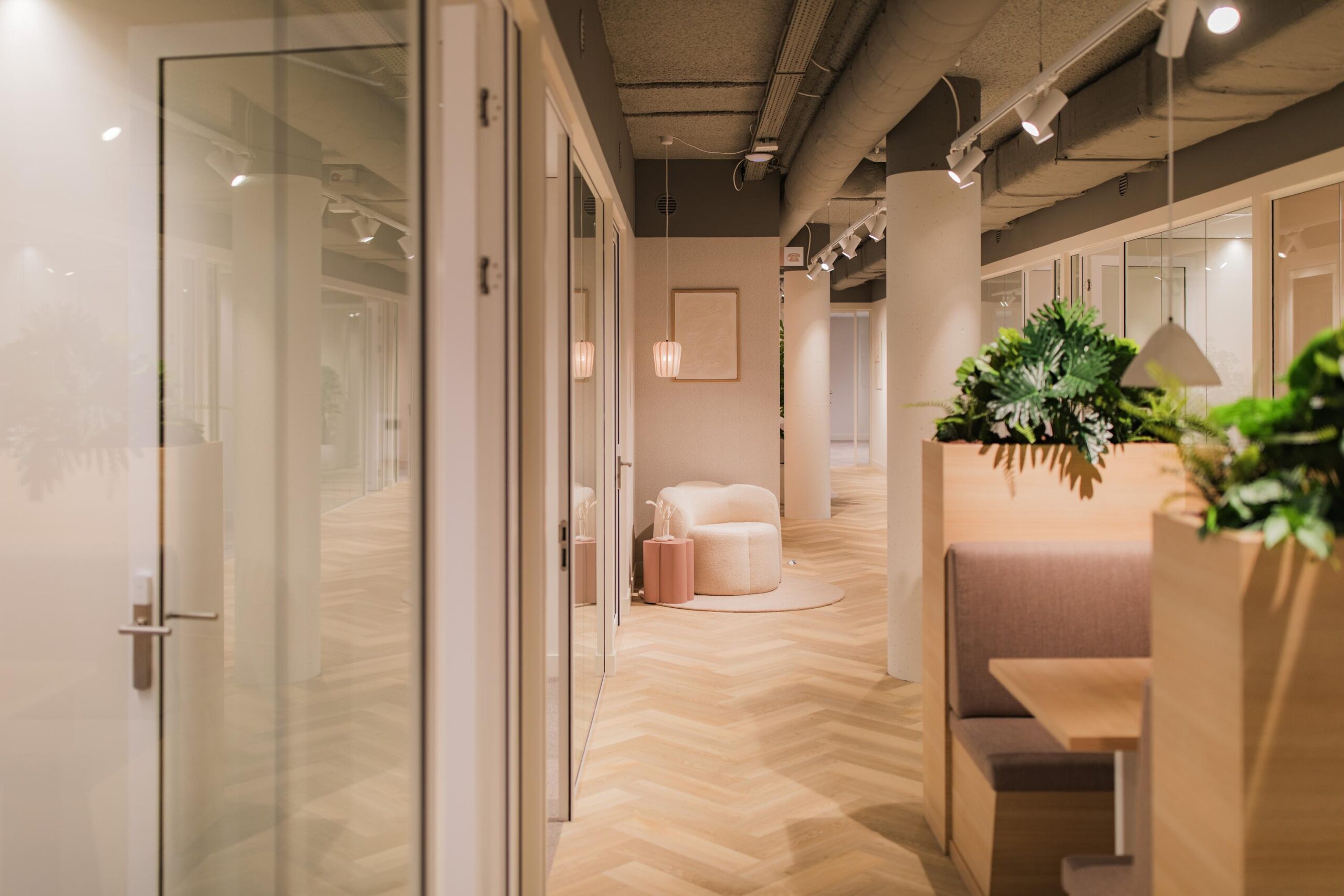 Modern office hallway at Hullenbergweg featuring soft lighting, wood flooring, indoor plants, and cozy seating areas.