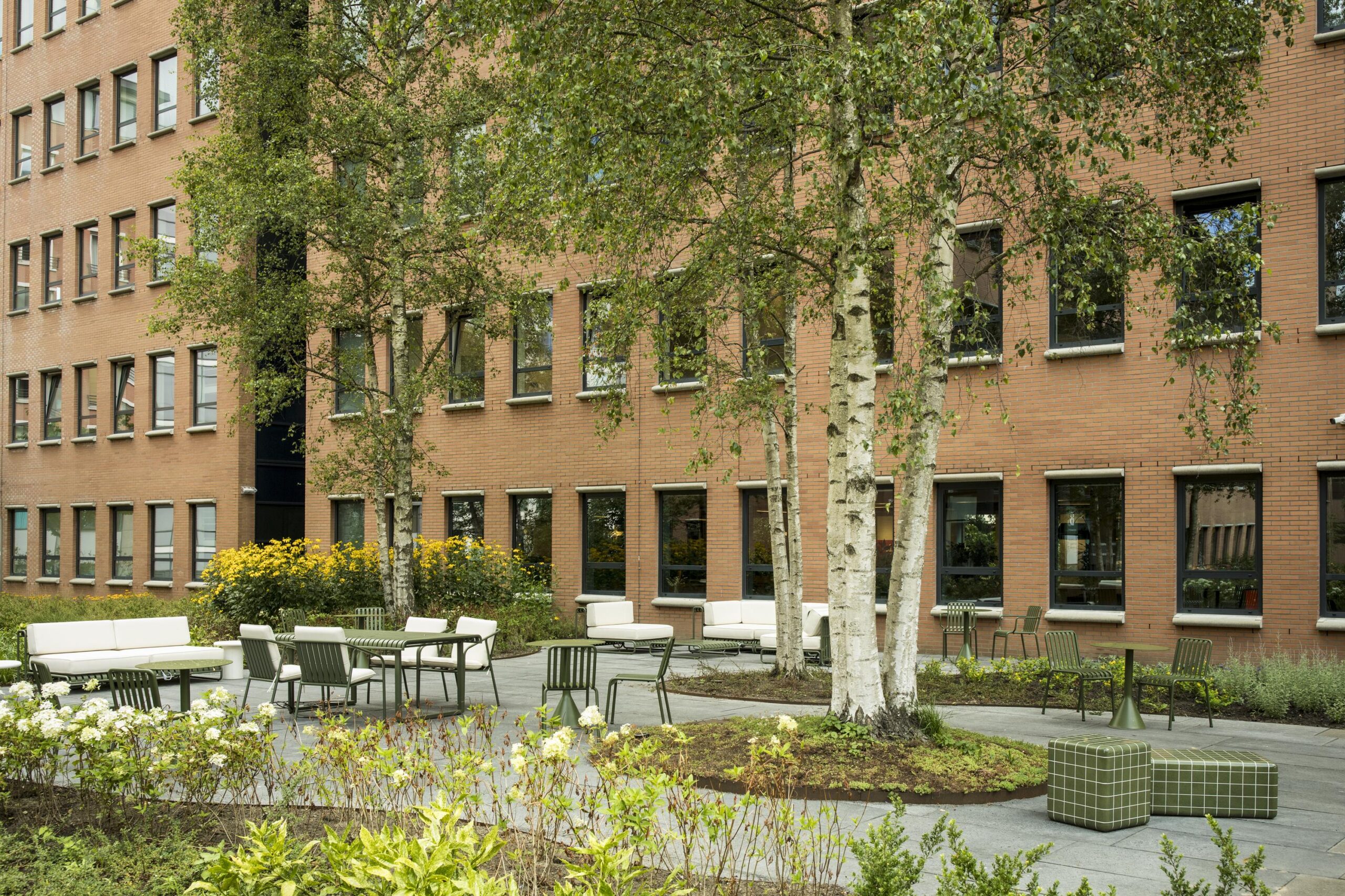 Outdoor seating area with modern furniture and greenery in front of a brick office building on Hullenbergweg.