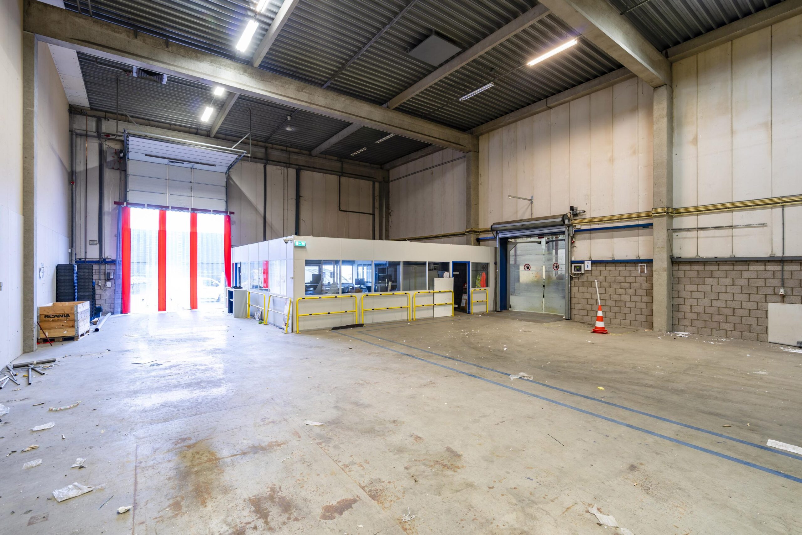 Een lege, ruime loods met een kantoorruimte en geopende overheaddeur aan de s-Gravelandseweg.