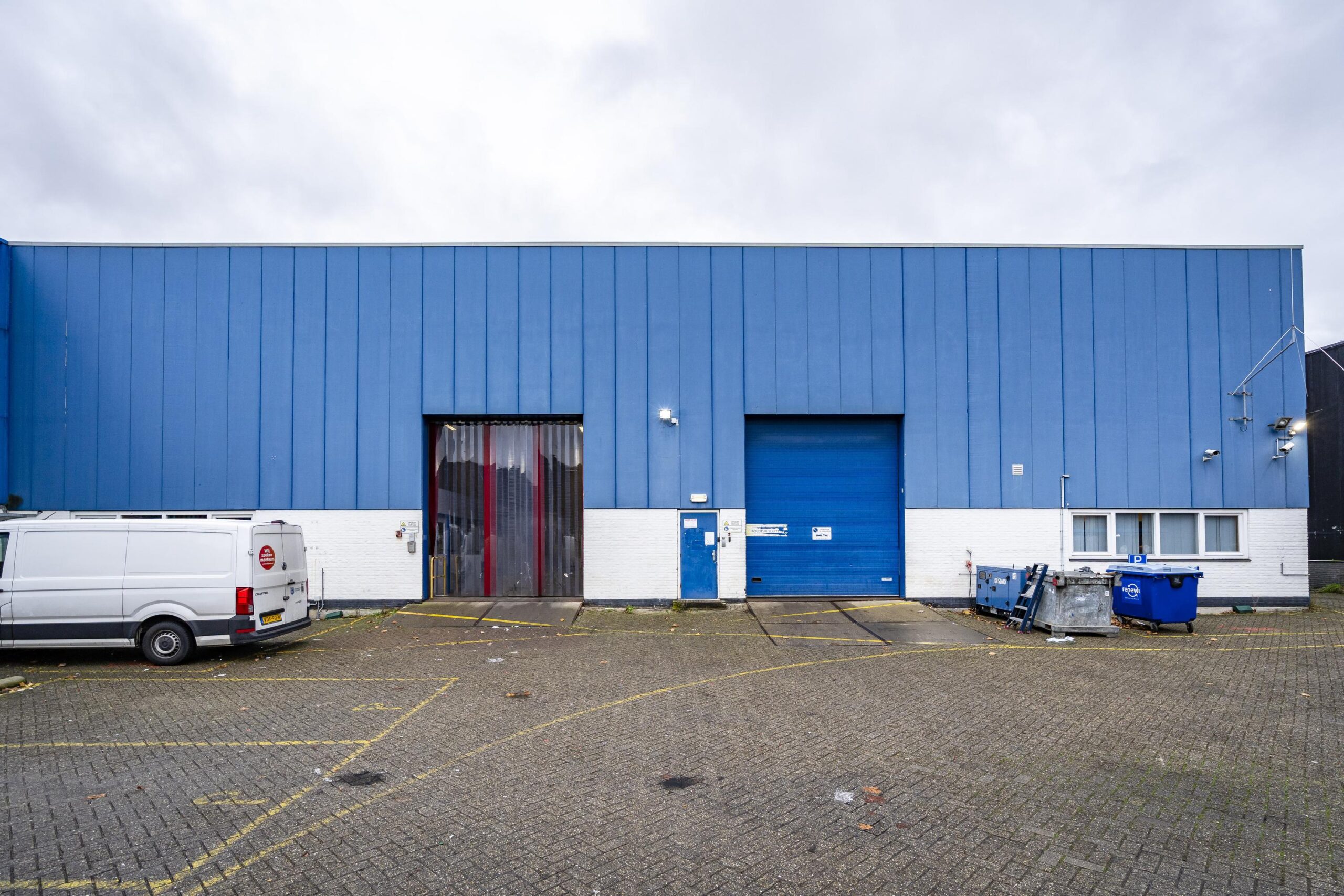 Een blauw industrieel gebouw aan de 's-Gravelandseweg met een witte bestelwagen geparkeerd ervoor.