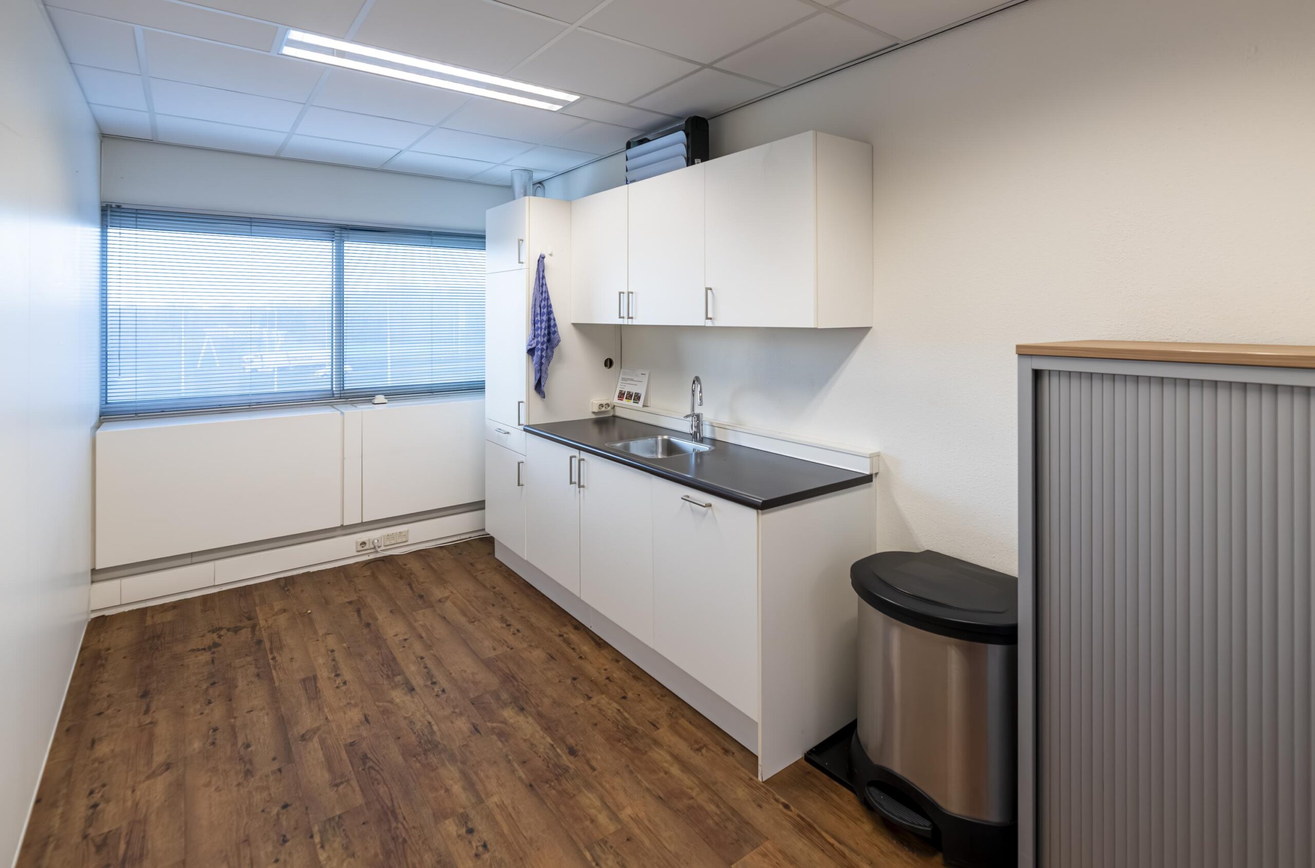 Kleine, moderne pantry met witte keukenkasten, donker aanrechtblad en houten vloer in een kantoor aan de Seattleweg.