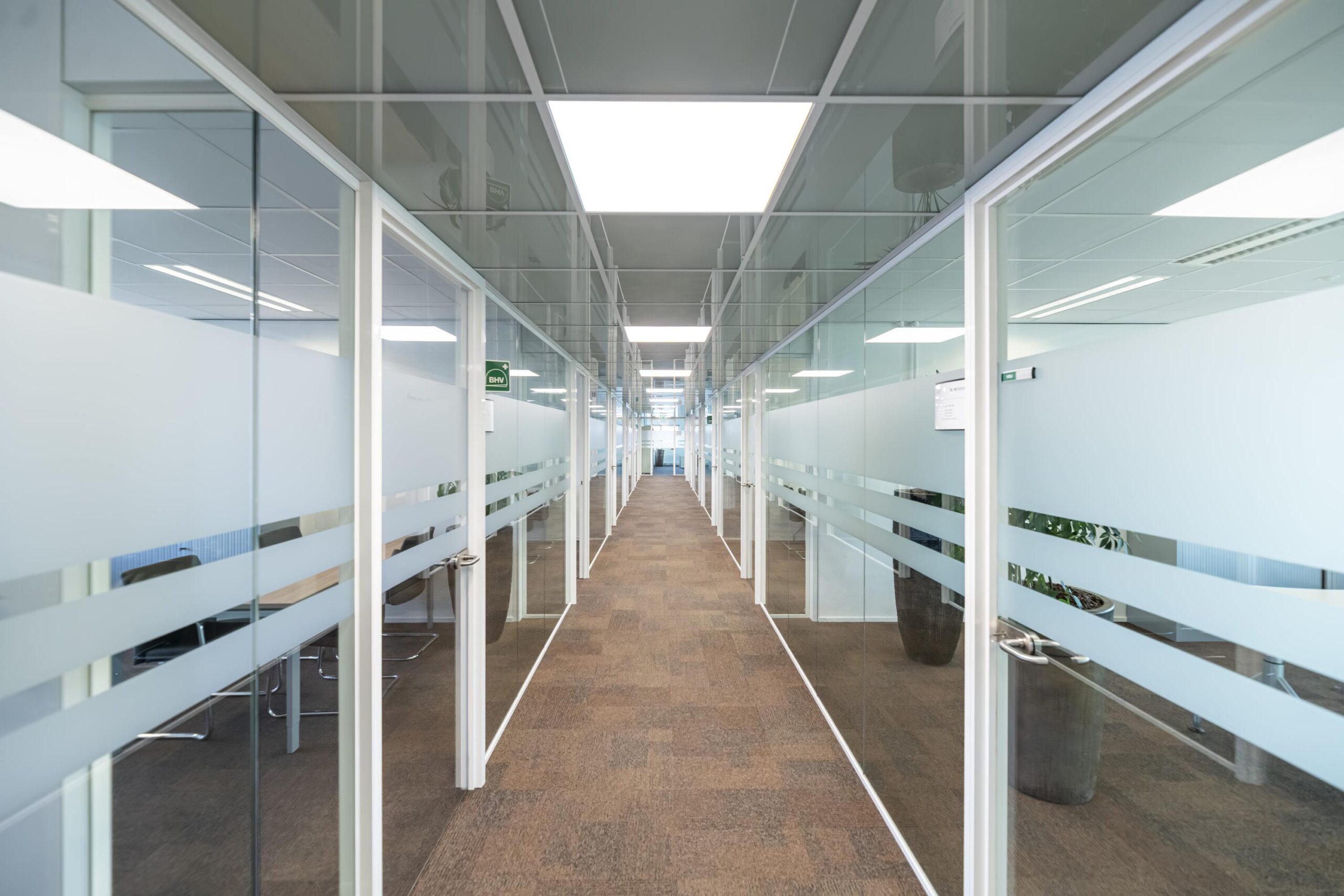Lange gang in een modern kantoorpand aan de Seattleweg met glazen kantoorwanden en vloerbedekking.