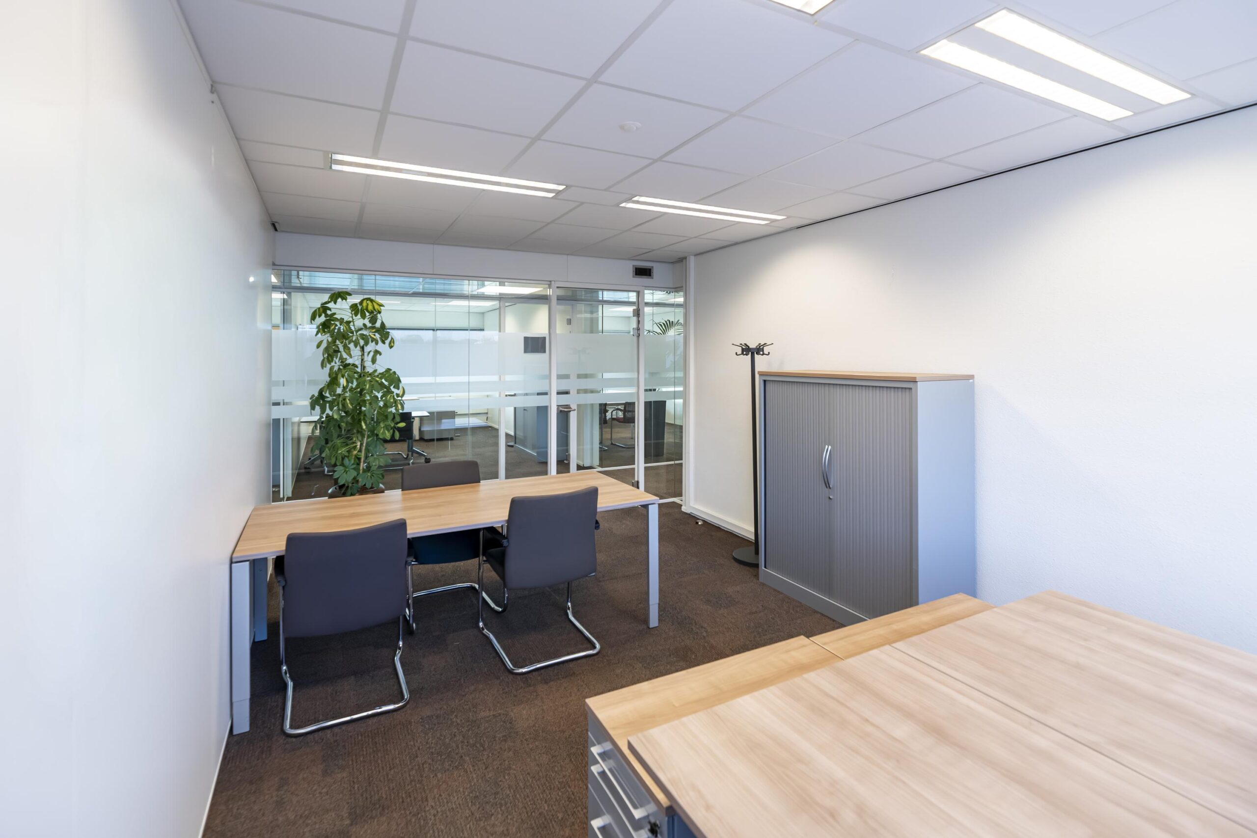 Moderne kantoorruimte aan de Seattleweg met bureaus, stoelen, een opbergkast en een glazen scheidingswand.