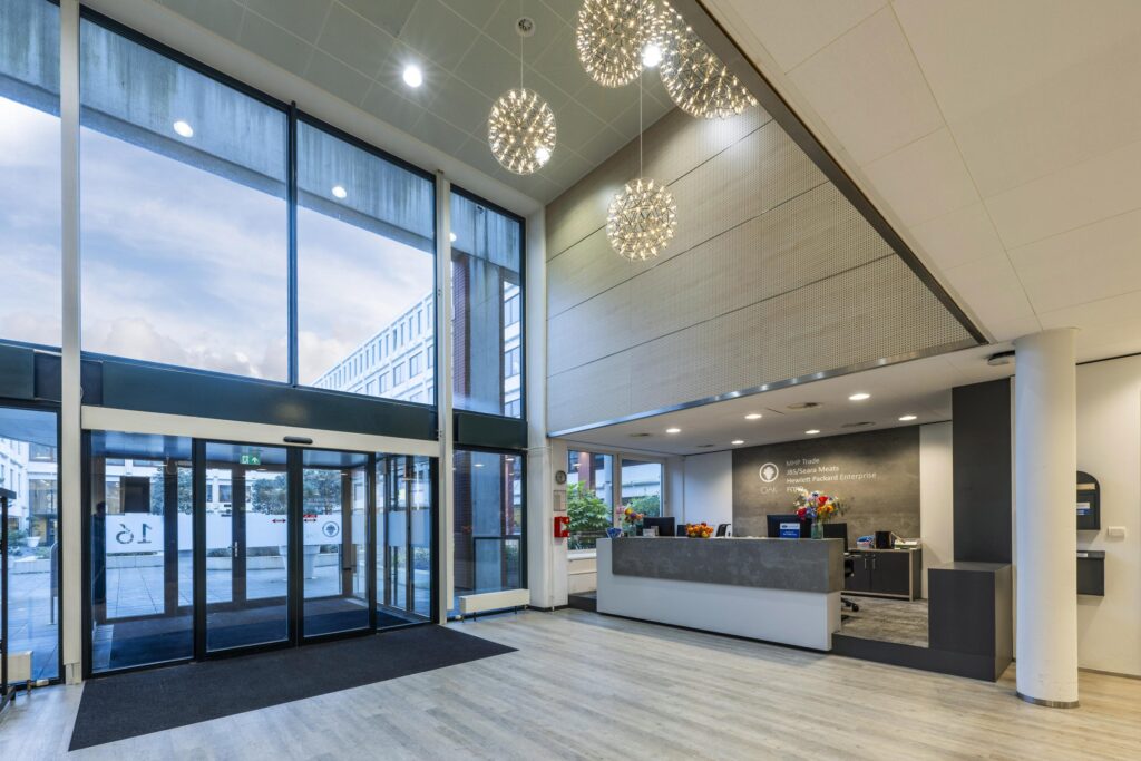 Moderne, lichte entreehal van een kantoorpand aan de Stroombaan met glazen schuifdeuren en een receptiebalie.