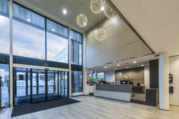 Moderne, lichte entreehal van een kantoorpand aan de Stroombaan met glazen schuifdeuren en een receptiebalie.