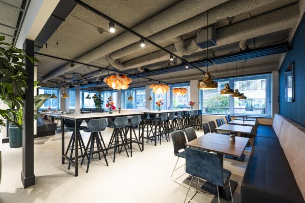 Moderne en sfeervolle bedrijfsrestaurant Stroombaan met hoge tafels, designlampen en blauwe zitmeubels.