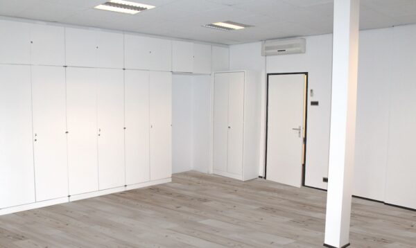 Lege, witte kamer met inbouwkasten, een deur en een airconditioning aan de muur in Oosteinde.