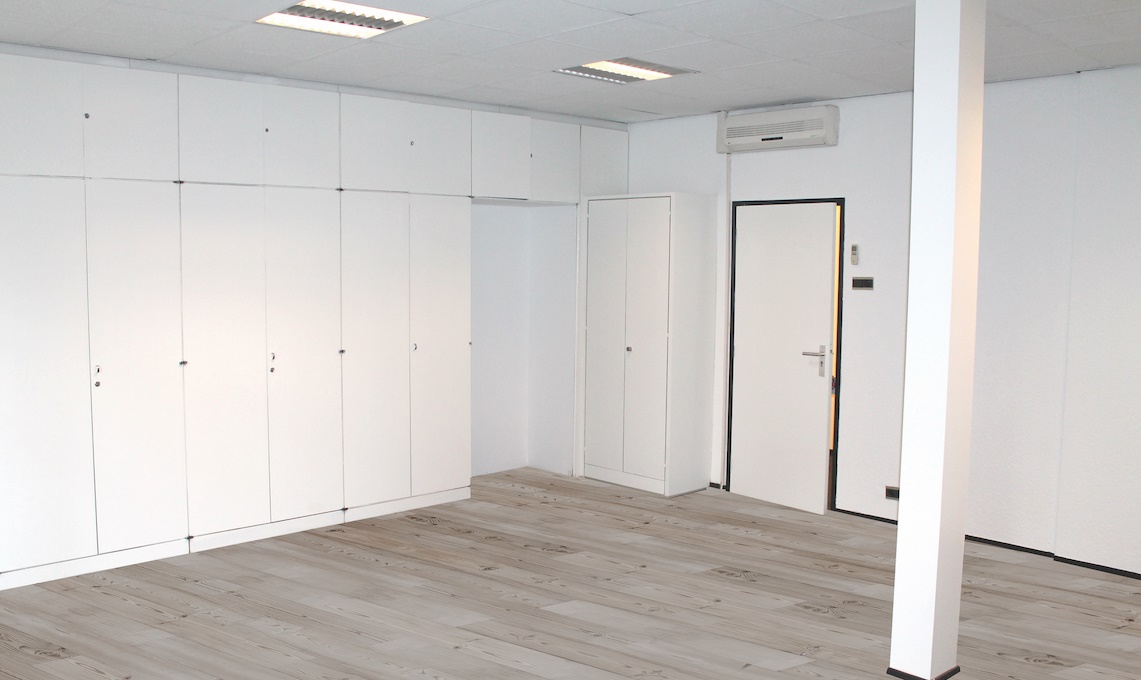 Lege, witte kamer met inbouwkasten, een deur en een airconditioning aan de muur in Oosteinde.