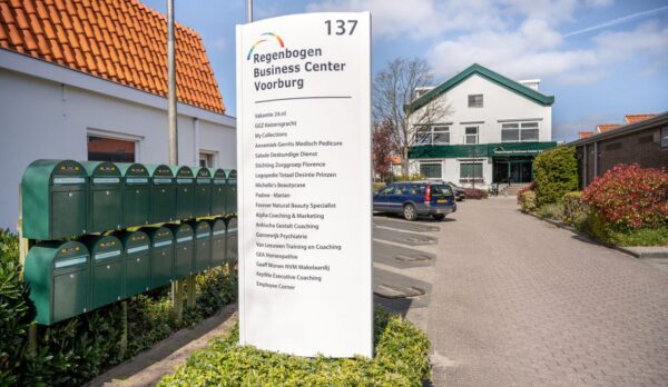 Ingang van Regenbogen Business Center Voorburg met een groot wit naambord en meerdere groene brievenbussen.