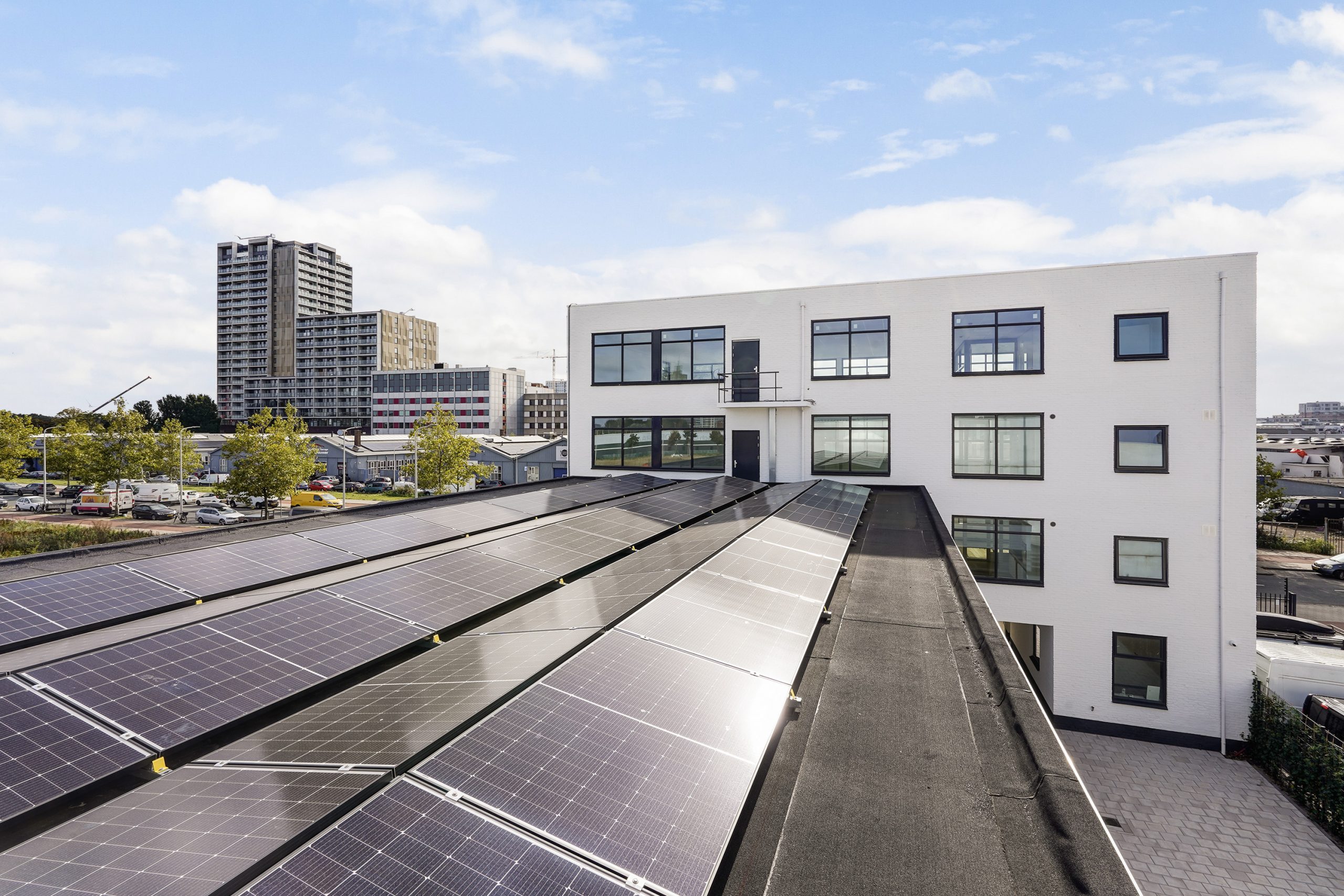 Wit bedrijfsgebouw aan de Mercuriusweg met zonnepanelen op het dak en hoogbouw op de achtergrond.