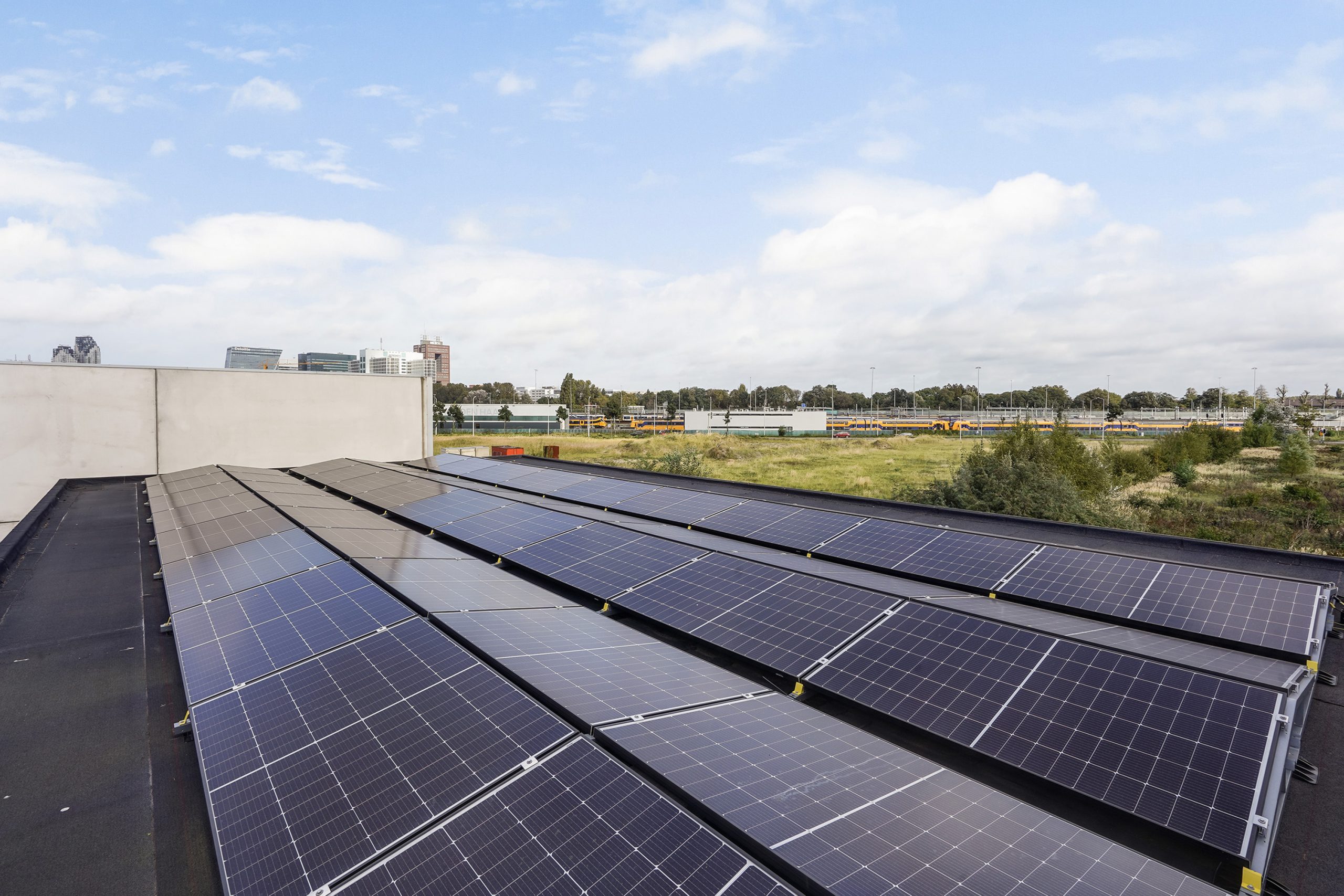 Zonnepanelen op het dak van een bedrijfsgebouw aan de Mercuriusweg met uitzicht op een industrieterrein en spoorlijn.