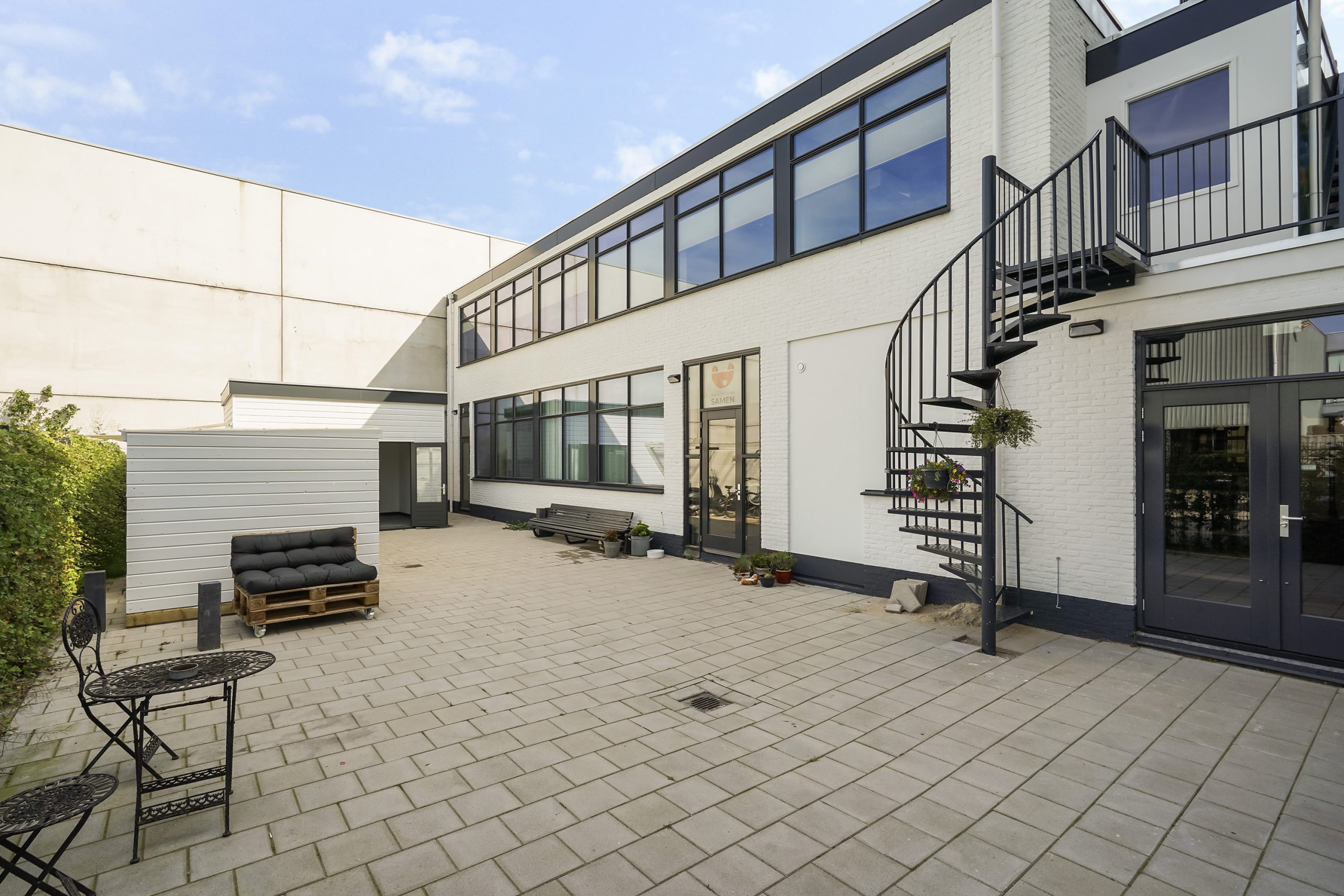 Binnenplaats van een modern bedrijfs- of kantoorpand aan de Mercuriusweg met een wenteltrap, zitgelegenheid en bestrate vloer.