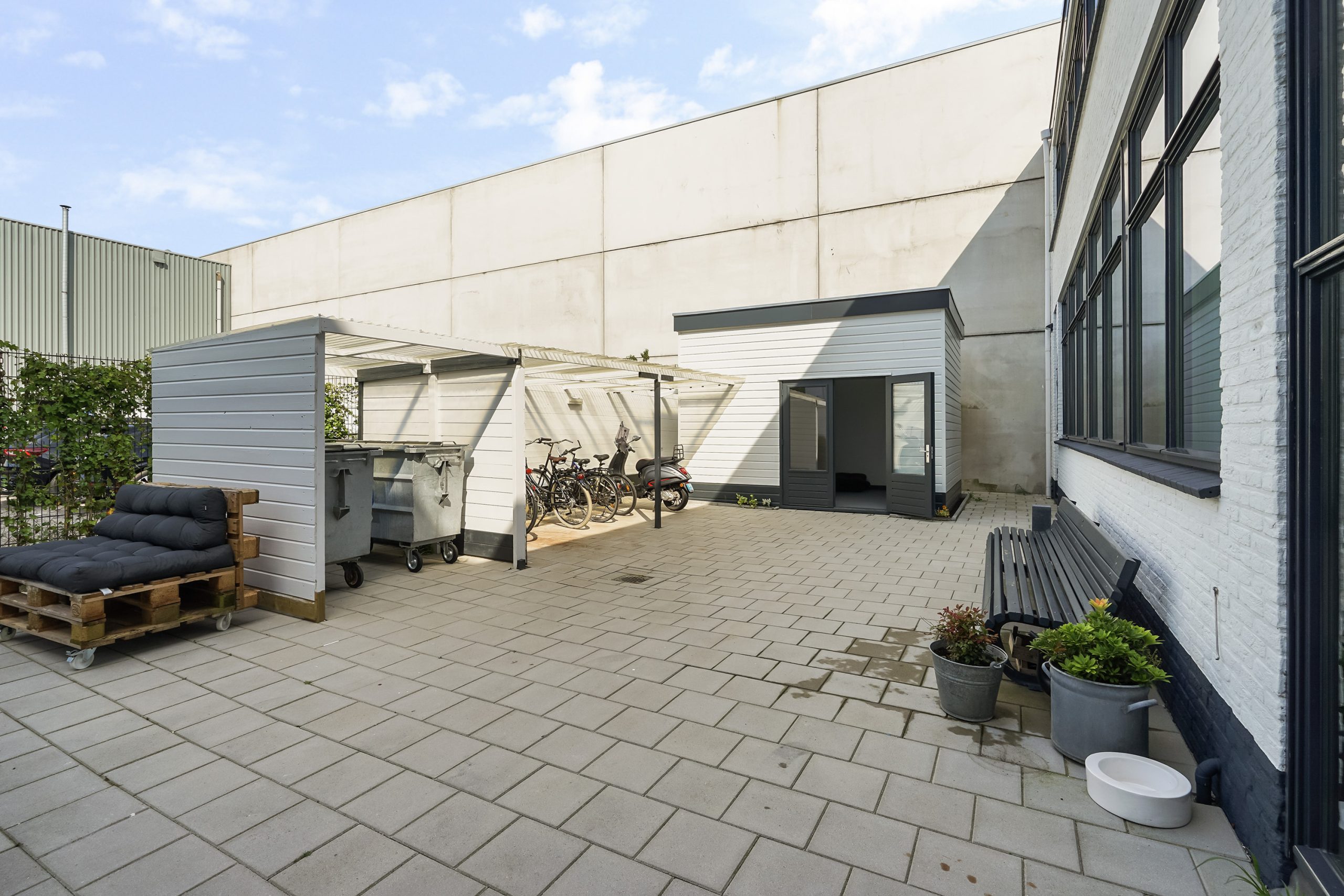 Grote, betegelde binnenplaats aan de Mercuriusweg met fietsenstalling, afvalcontainers, tuinbank en palletbank.