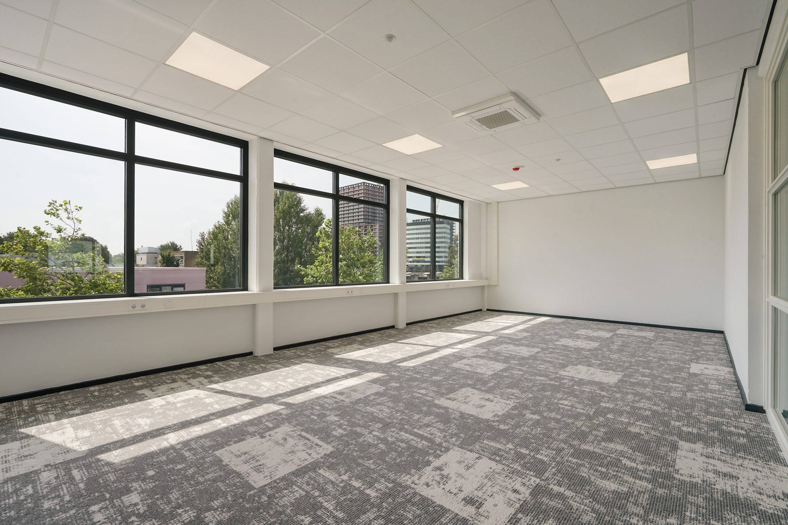 Licht en modern leeg kantoor met grote ramen aan de Mercuriusweg en uitzicht op omliggende gebouwen en groen.