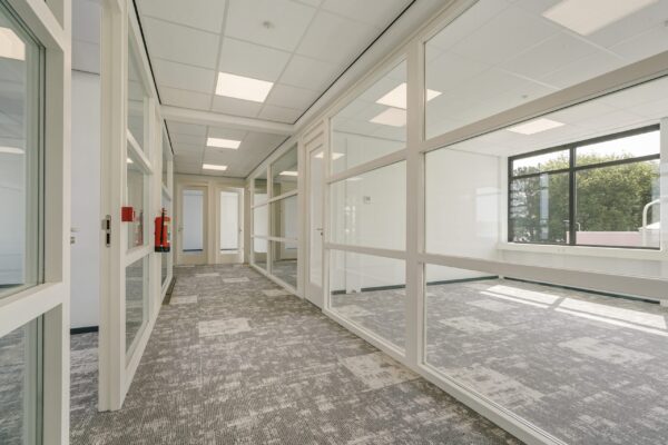 Lichte kantoorruimte aan de Mercuriusweg met glazen scheidingswanden en grijs tapijt.