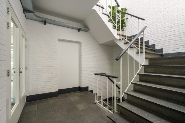 Moderne trappenhal in een gebouw aan de Mercuriusweg met witte bakstenen muren en donkergrijze stenen trap.