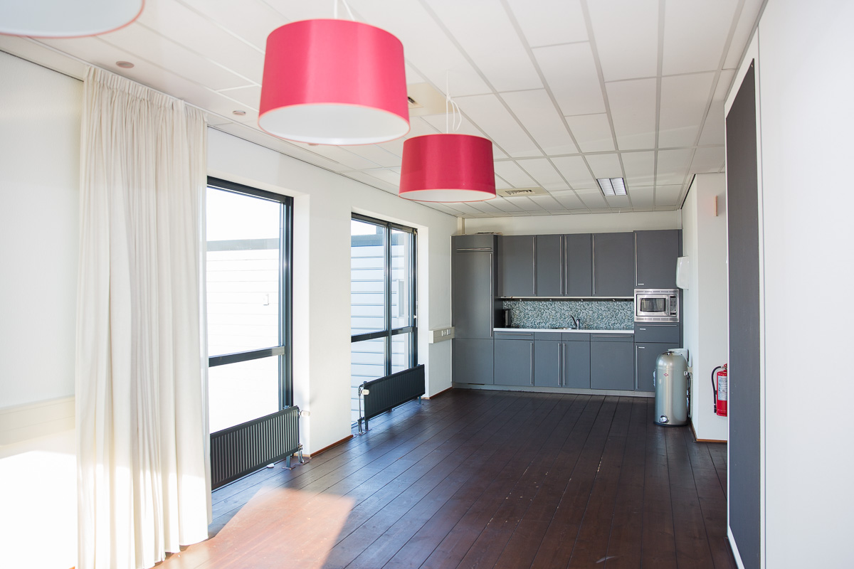 Moderne kantoorkeuken aan de Laan van s-Gravenmade met grijze kasten, houten vloer en roze hanglampen.