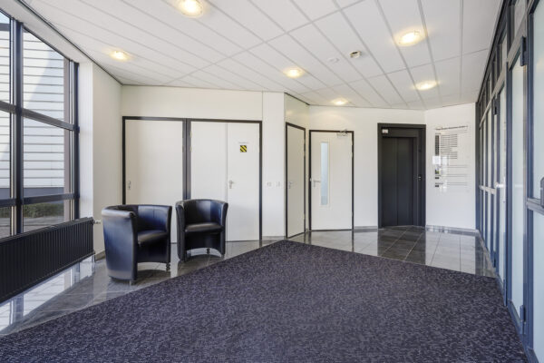 Ingangshal van een modern kantoorpand aan de Laan van s-Gravenmade met stoelen, lift en deuren naar verschillende ruimtes.