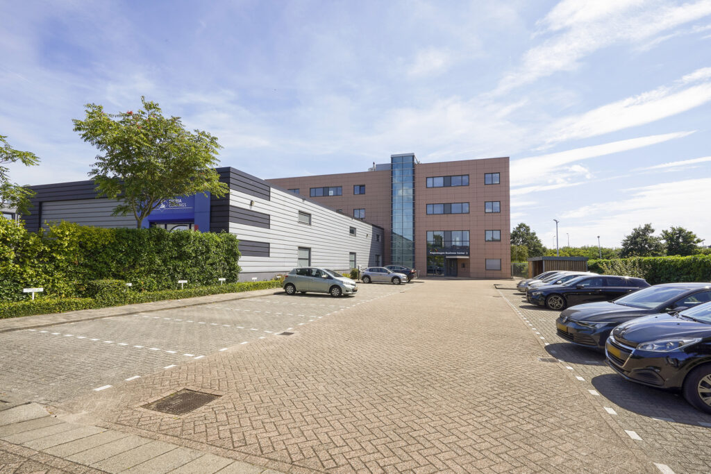 Kantoorpand aan de Laan van ’s-Gravenmade met parkeerplaatsen en geparkeerde auto's op een zonnige dag.